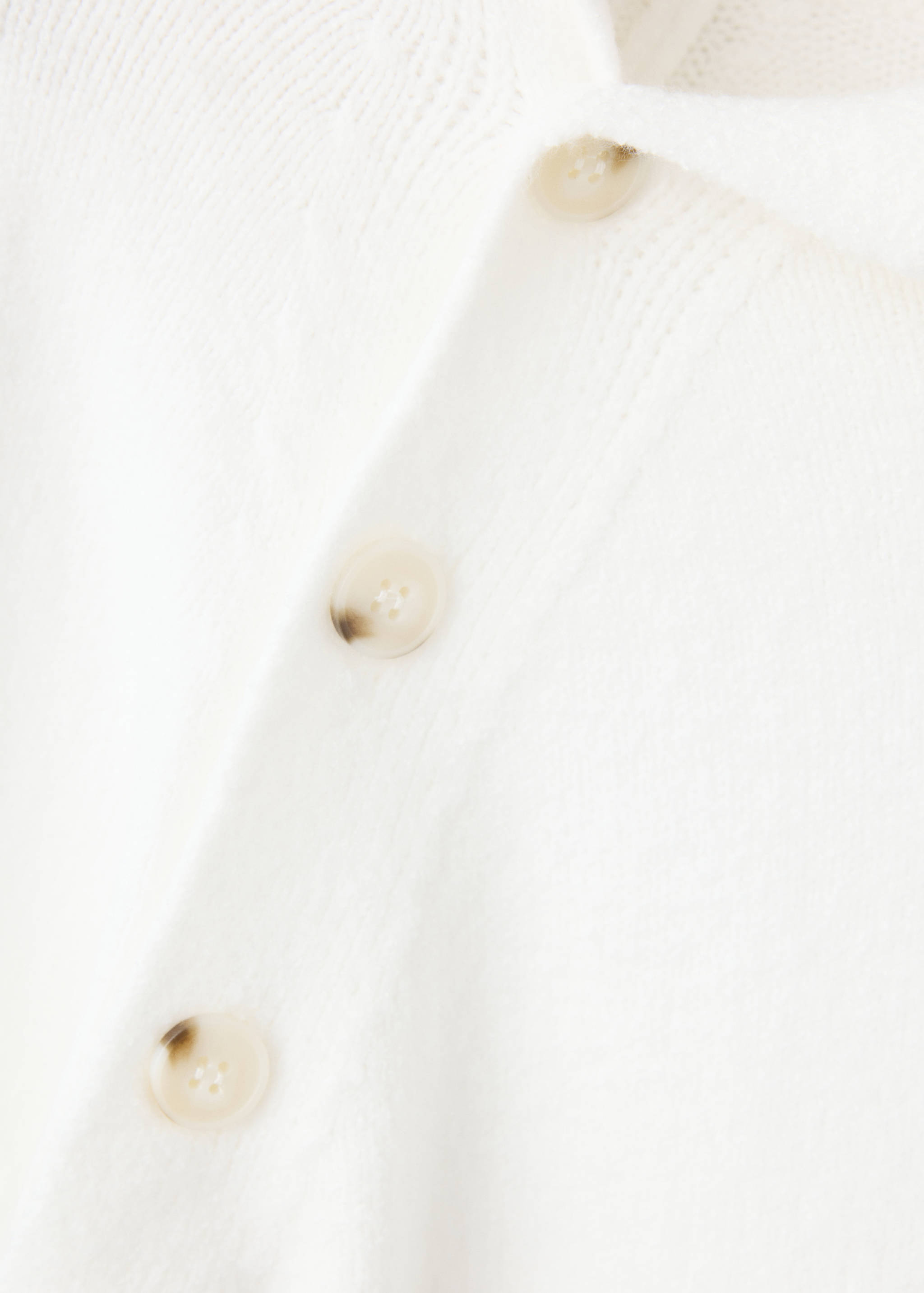 Close-up of white knitted jumper detail with tortoiseshell buttons.