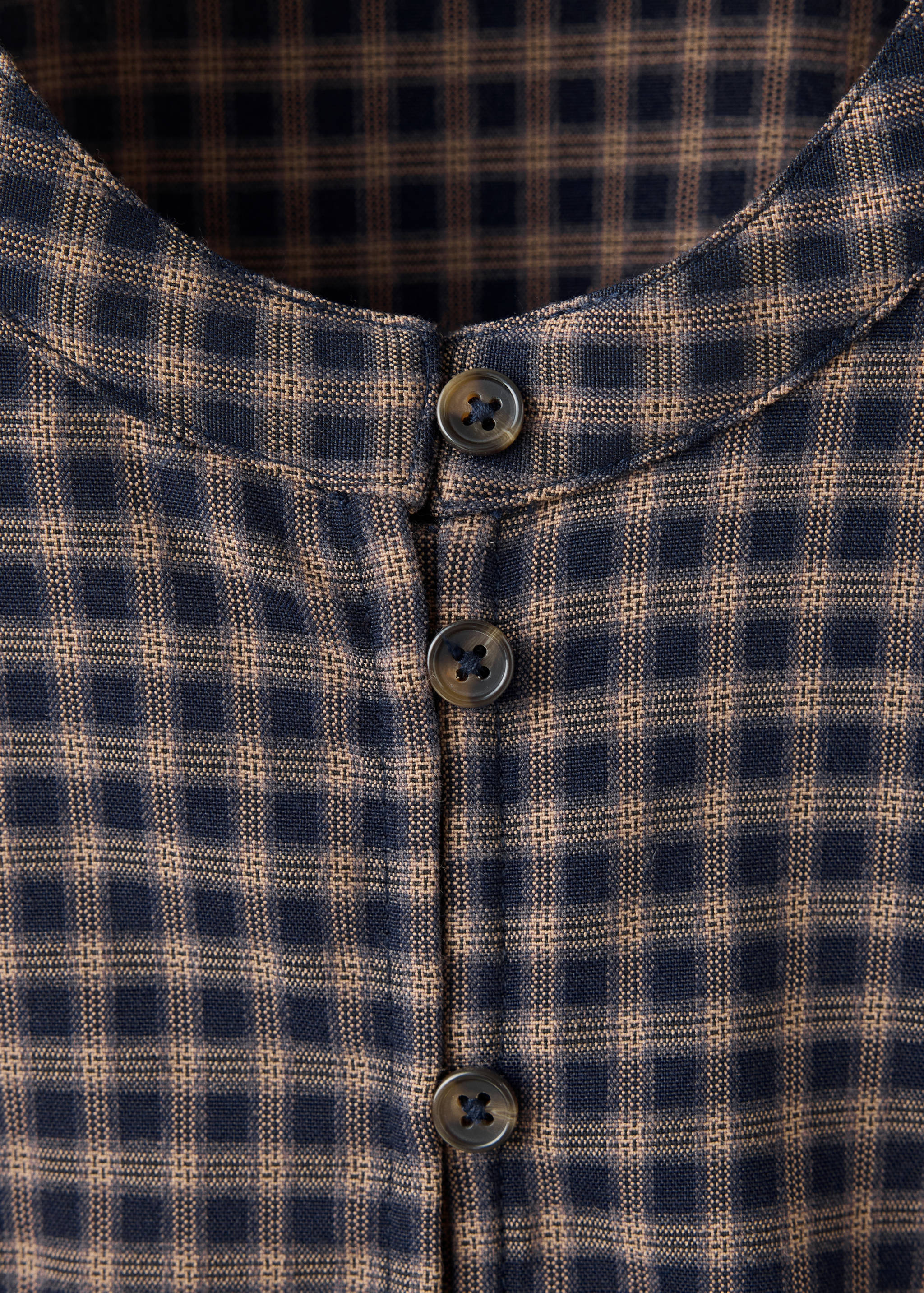 Checkered shirt detail showing the rounded neckline and button placket.