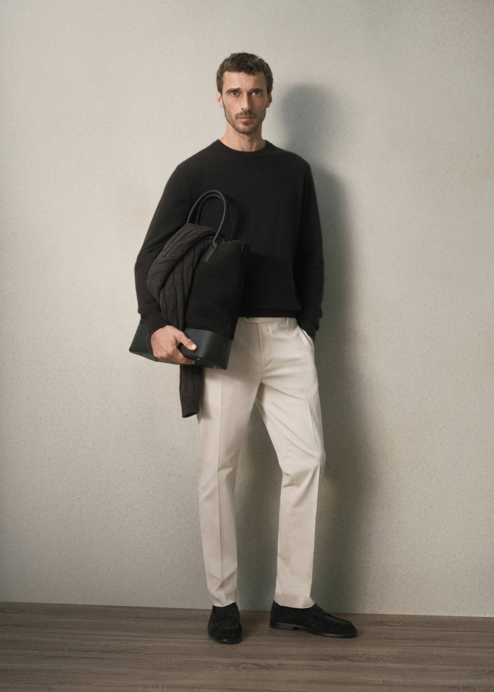 Light beige tailored trousers worn with a dark brown sweater and tote bag.