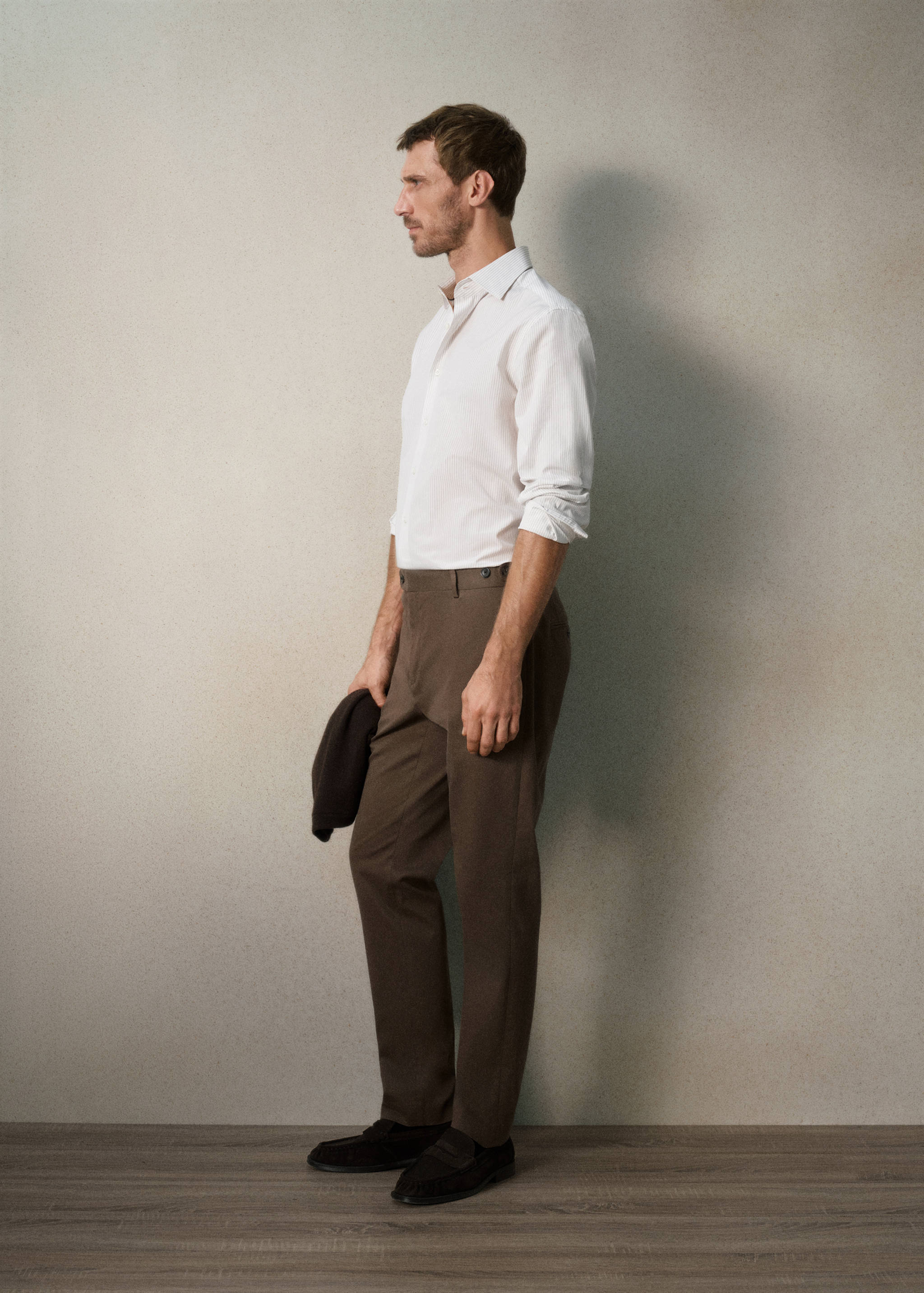 Brown straight-leg trousers worn with a white shirt and dark loafers.
