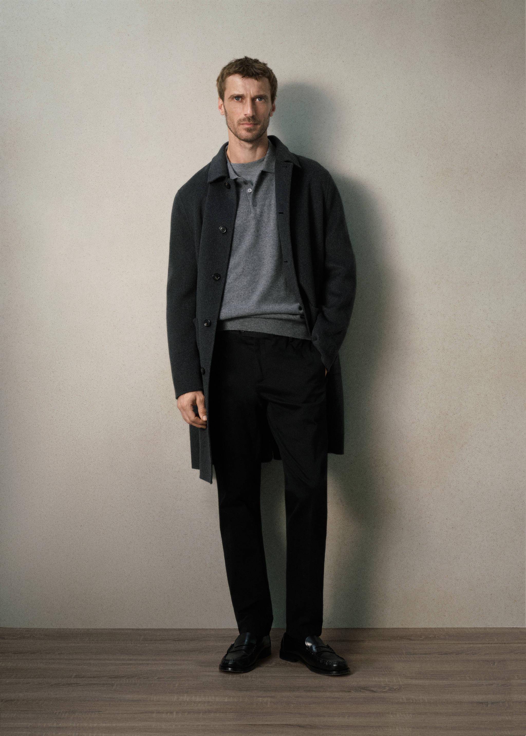 Black trousers with straight fit, styled with a grey knit polo and dark coat.