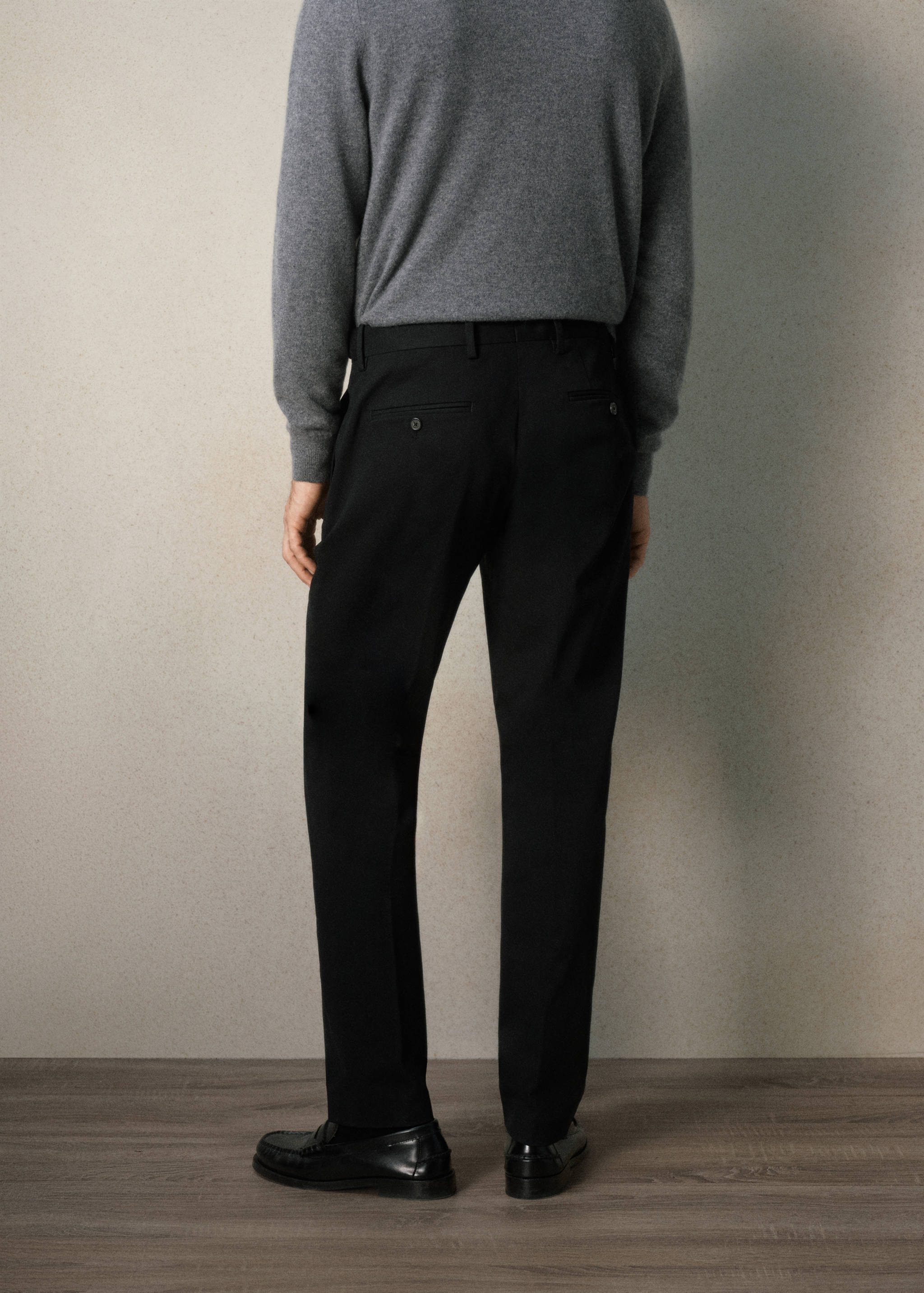 Back view of black tailored trousers with belt loops and buttoned welt pockets.