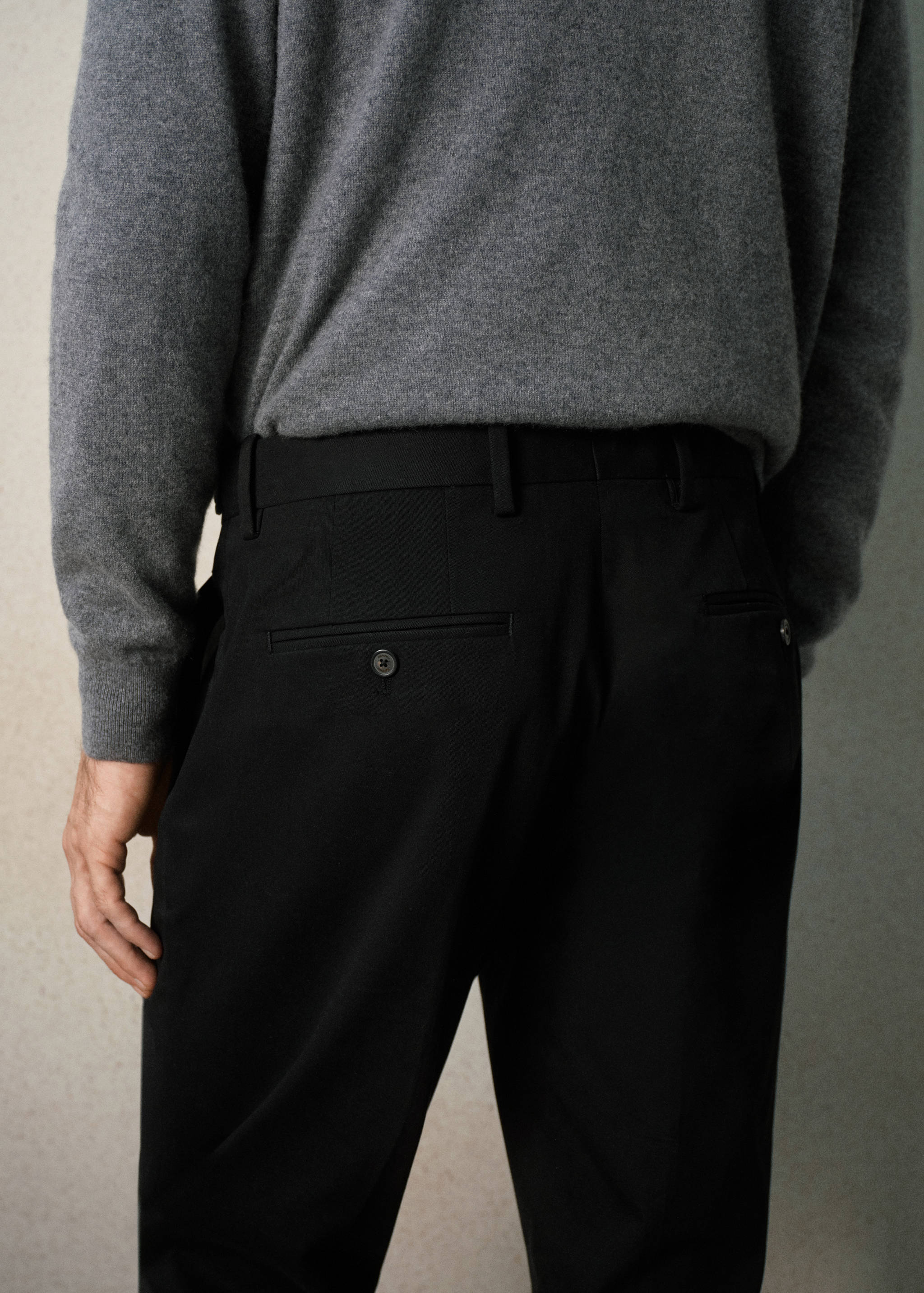 Black trousers featuring belt loops and back welt pockets, worn by a model.