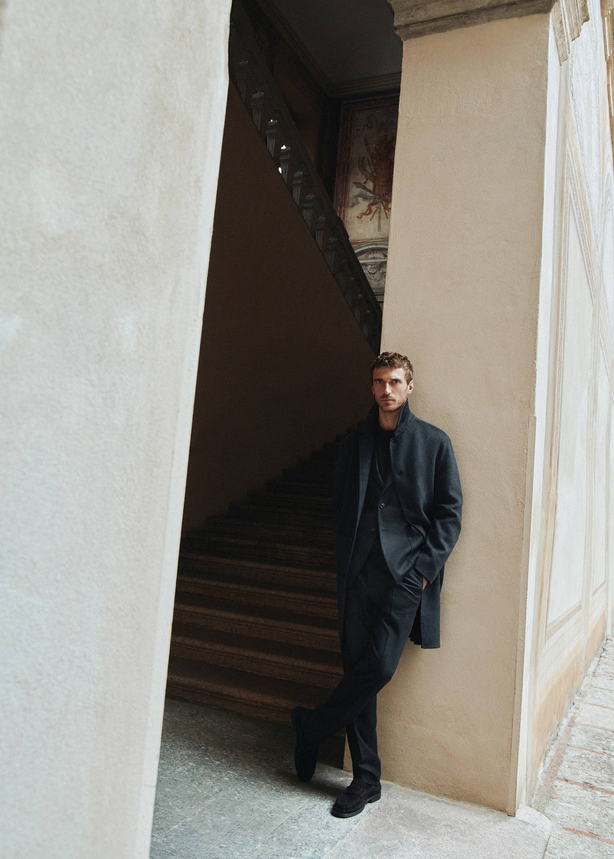 Dark grey trousers worn as part of a tailored suit with a matching blazer and overcoat.