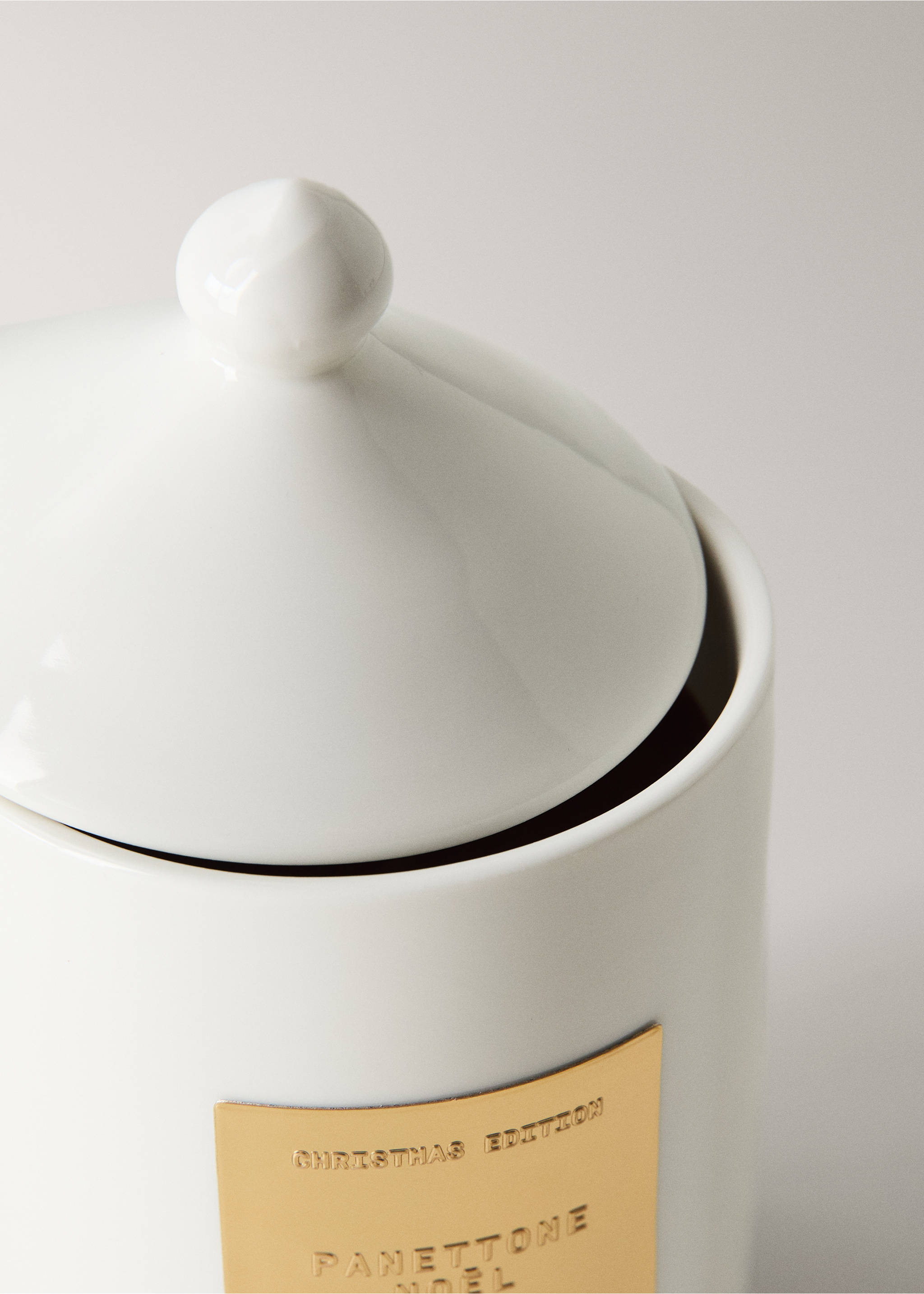 Close-up of a white ceramic candle container with a lid and gold label., Gold. Ref: 37028640-00.