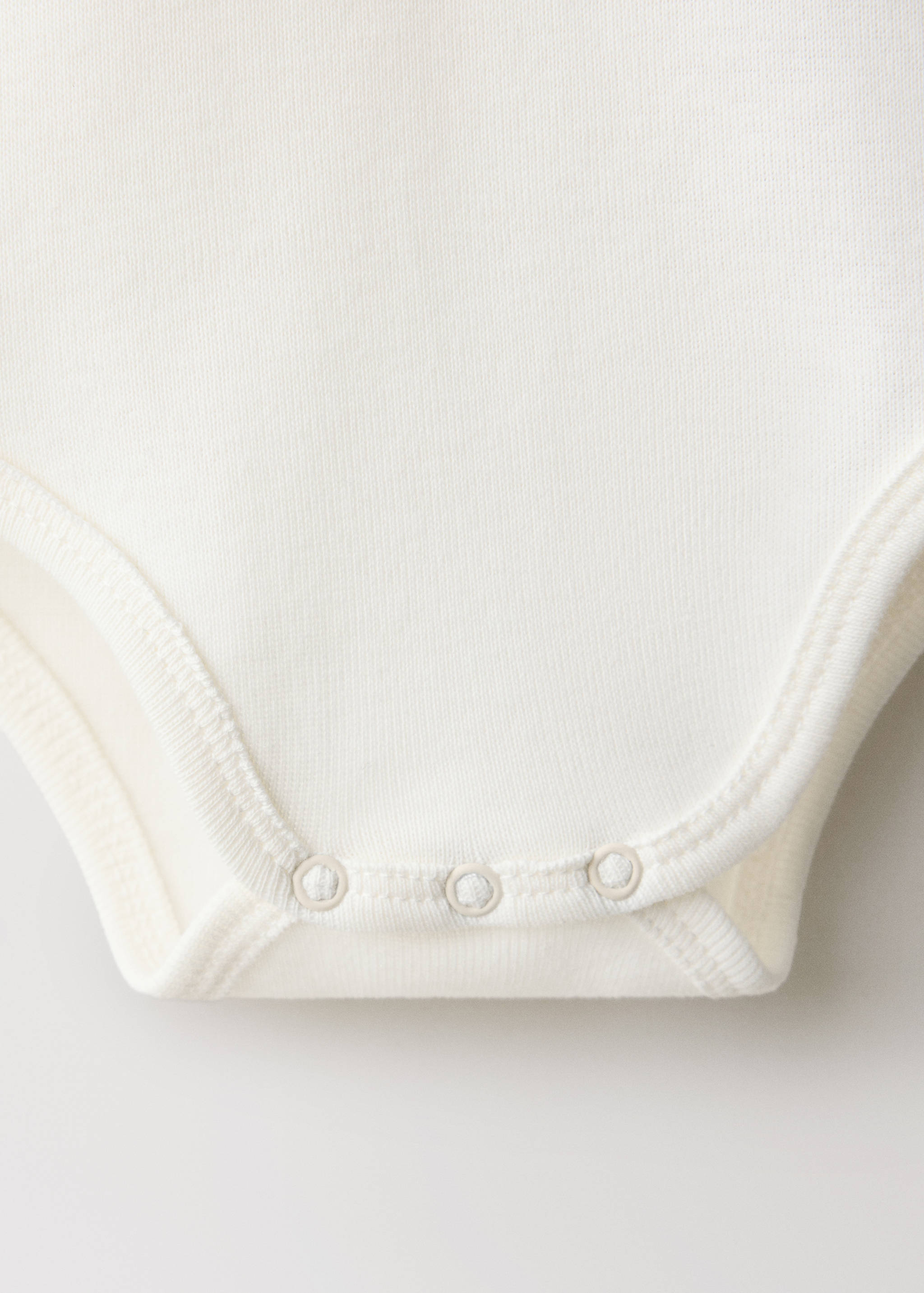 Off-white baby body detail showing the bottom snap closure.