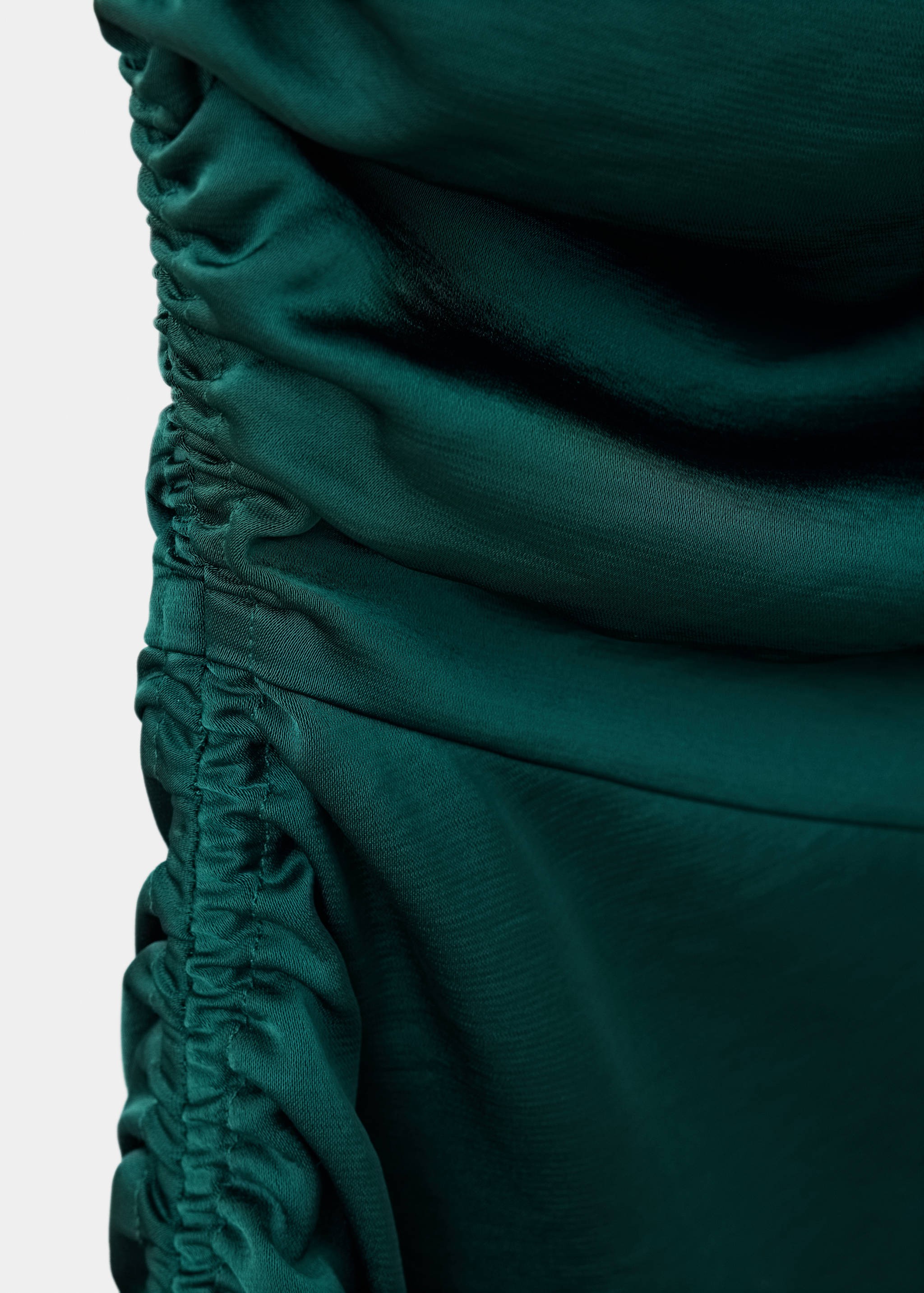 Close-up of a dark green dress featuring gathered ruched side detailing and satin fabric texture.