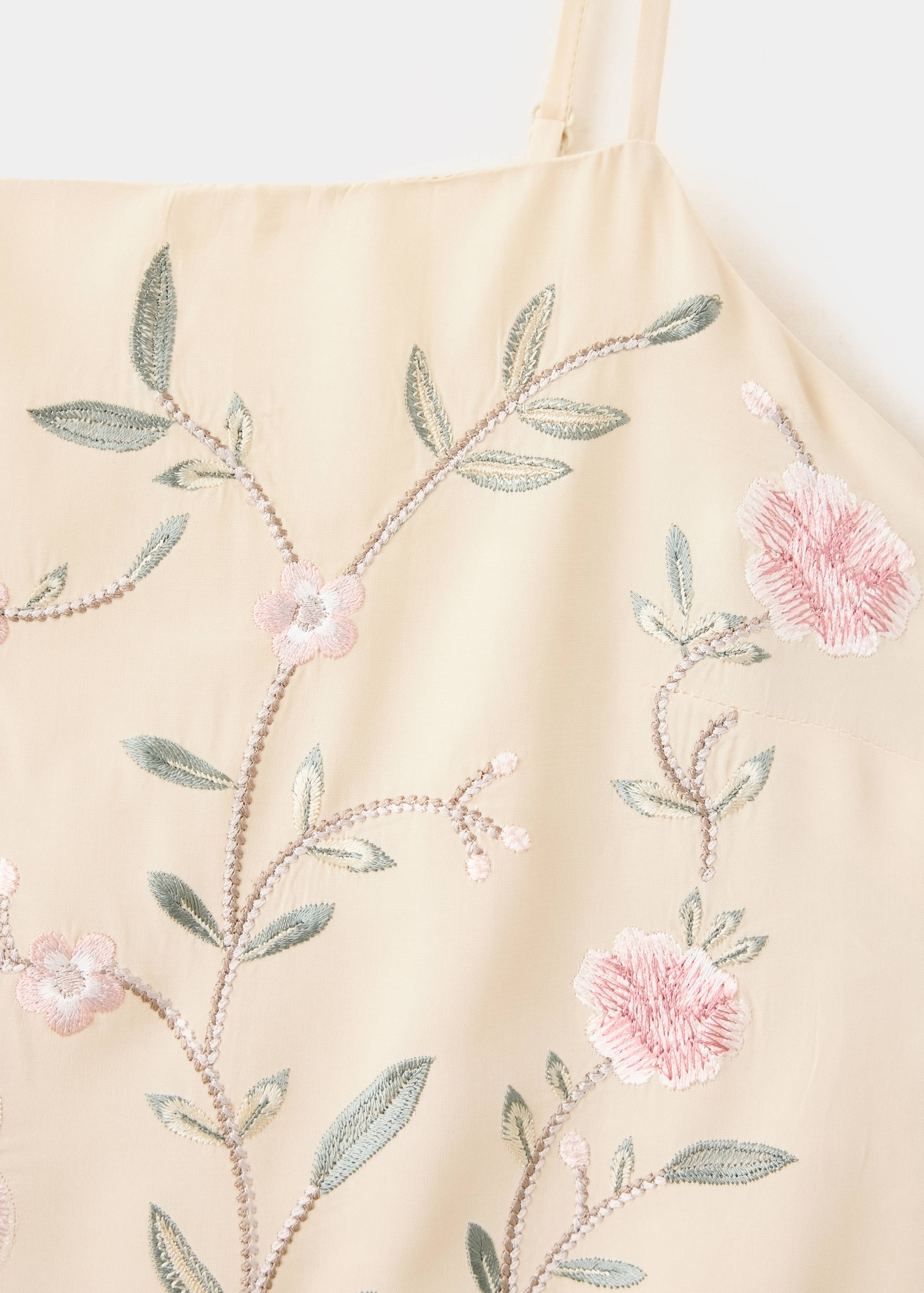 Close-up of a pale yellow dress with floral embroidery and thin straps.