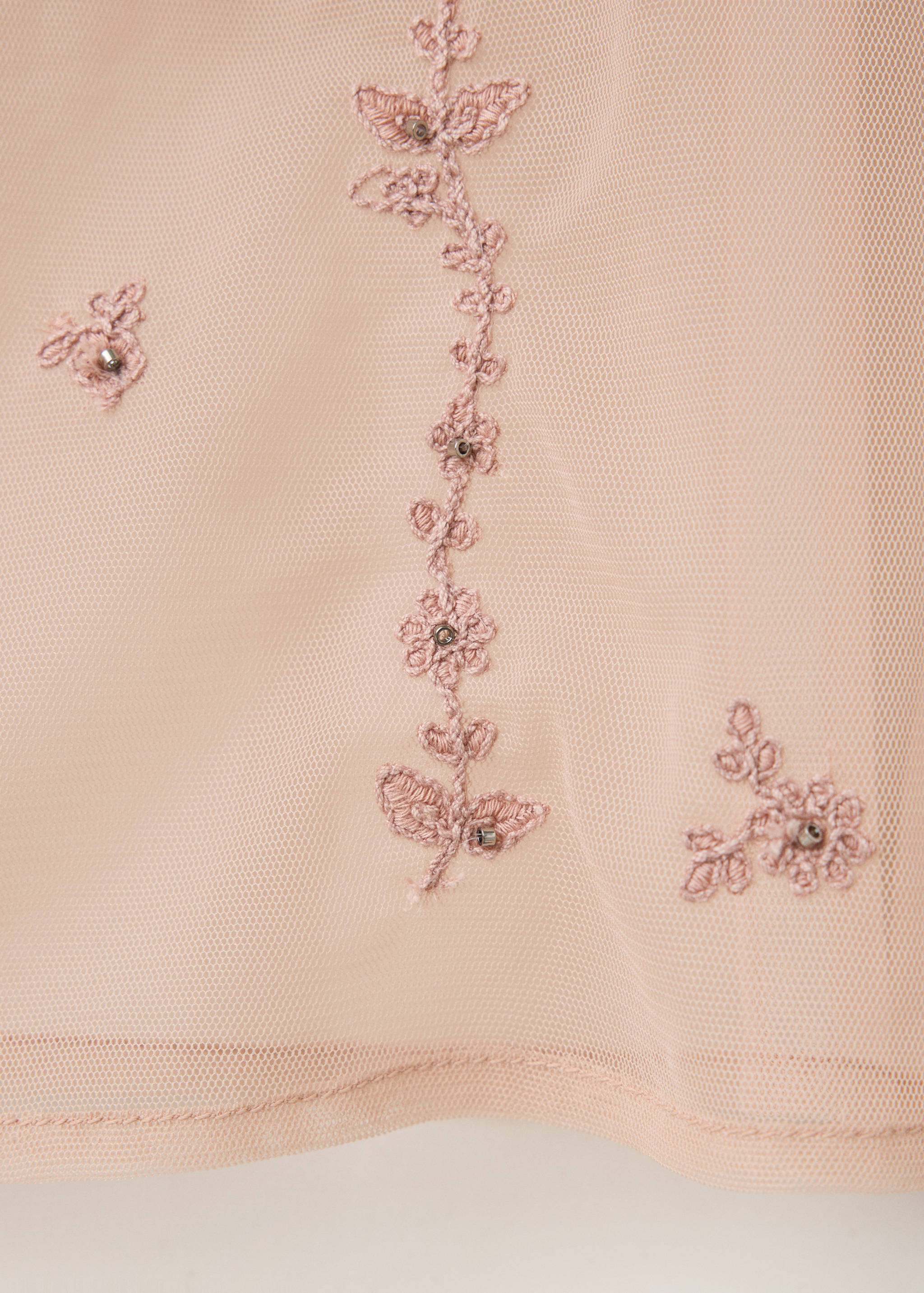 Detalle de blusa rosa de rejilla con bordado floral y abalorios.