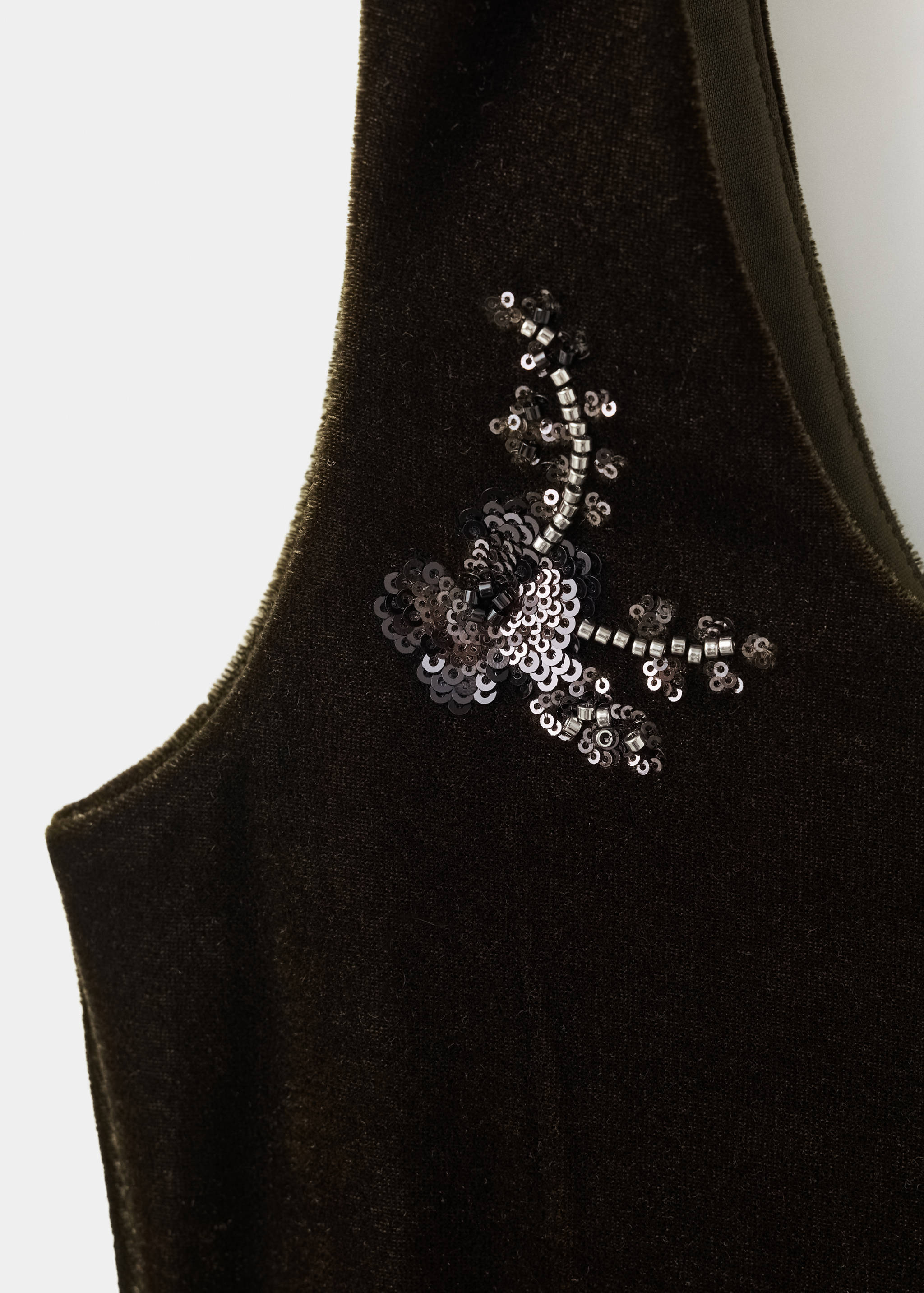 Close-up of a dark olive green velvet top with a beaded floral applique detail.