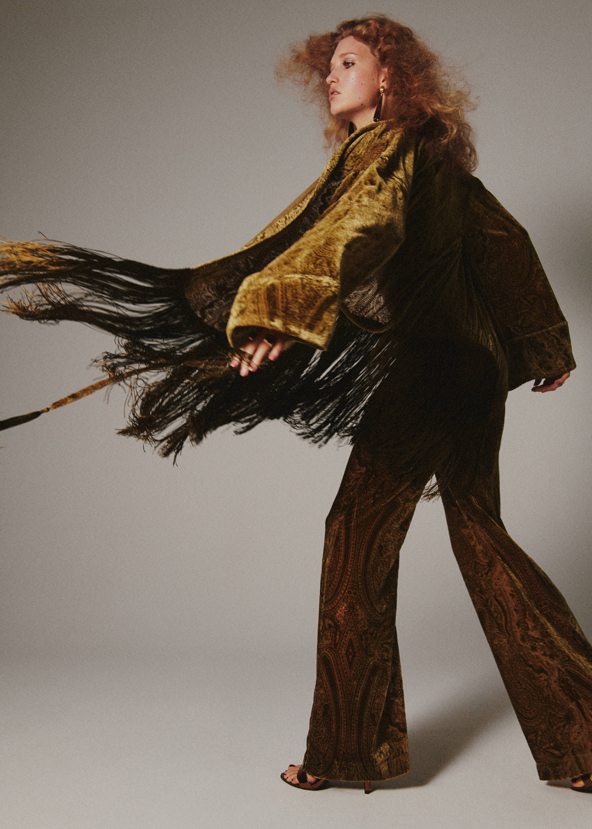 Olive green velvet poncho with long black fringe, worn with matching patterned trousers.