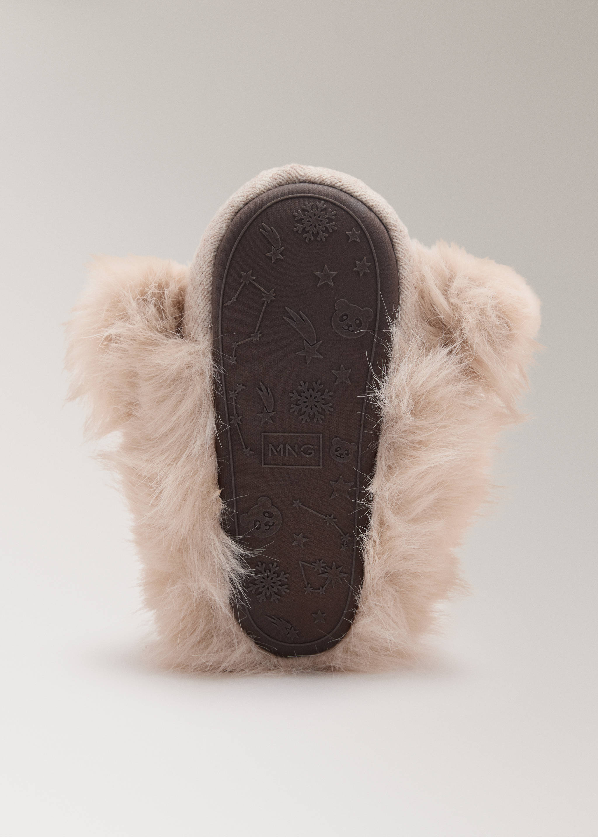 Primer plano de la suela de zapatilla infantil de goma marrón con dibujo, logotipo y ribete de efecto pelo beige.