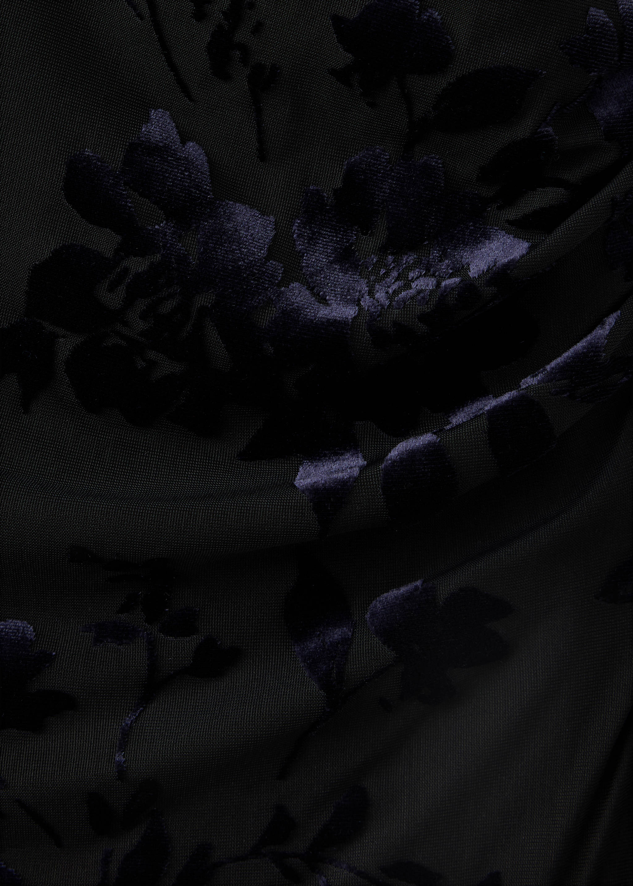 Close-up of black fabric with a dark blue flocked velvet floral pattern.
