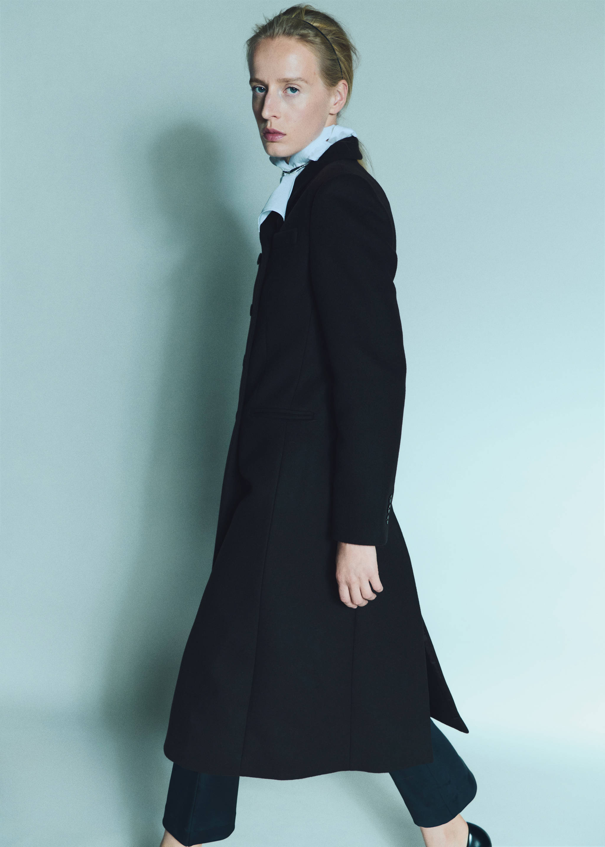 Long black tailored coat with a lapel collar and button fastening.