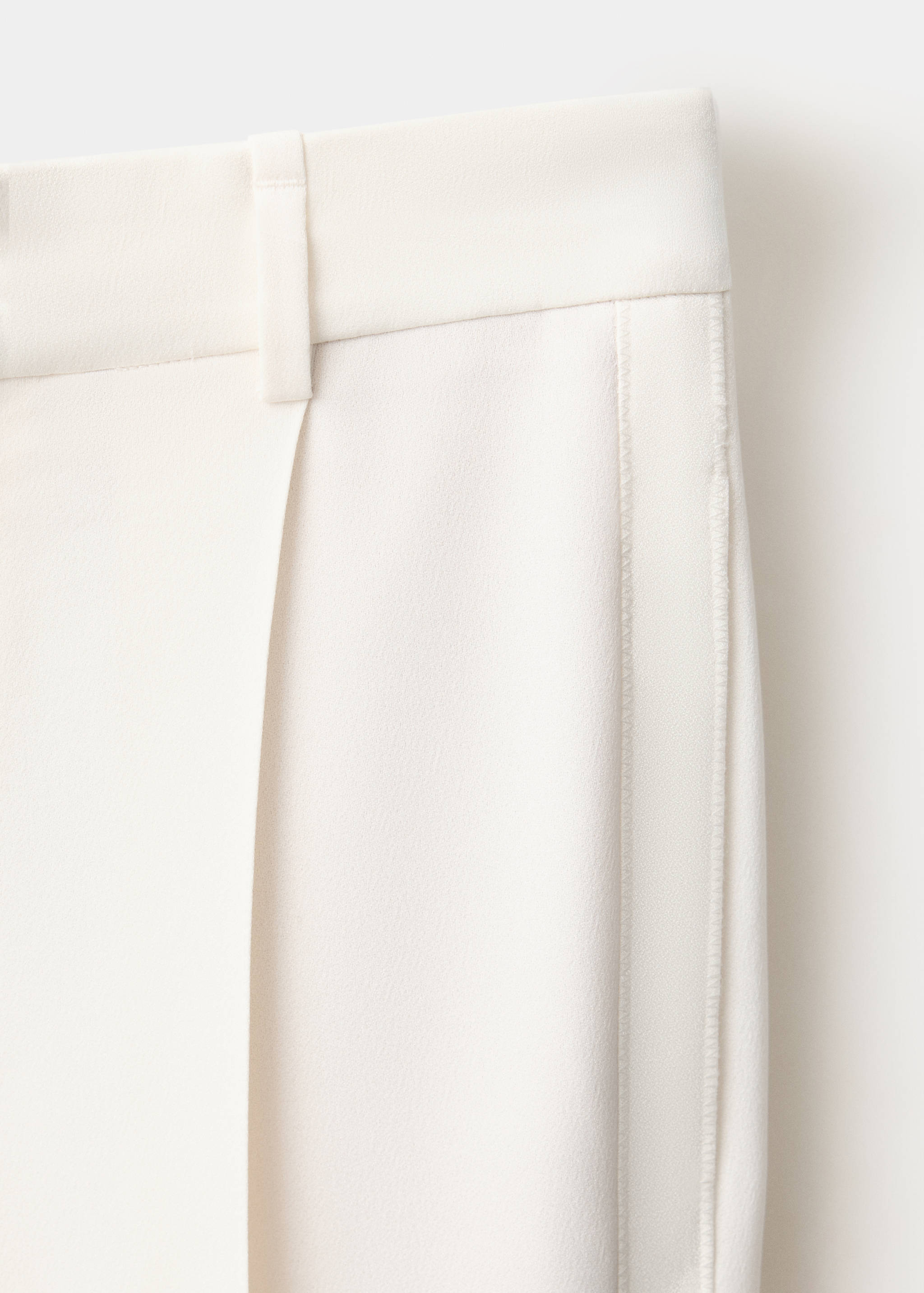Cream trousers fabric detail showing waistband and belt loop.
