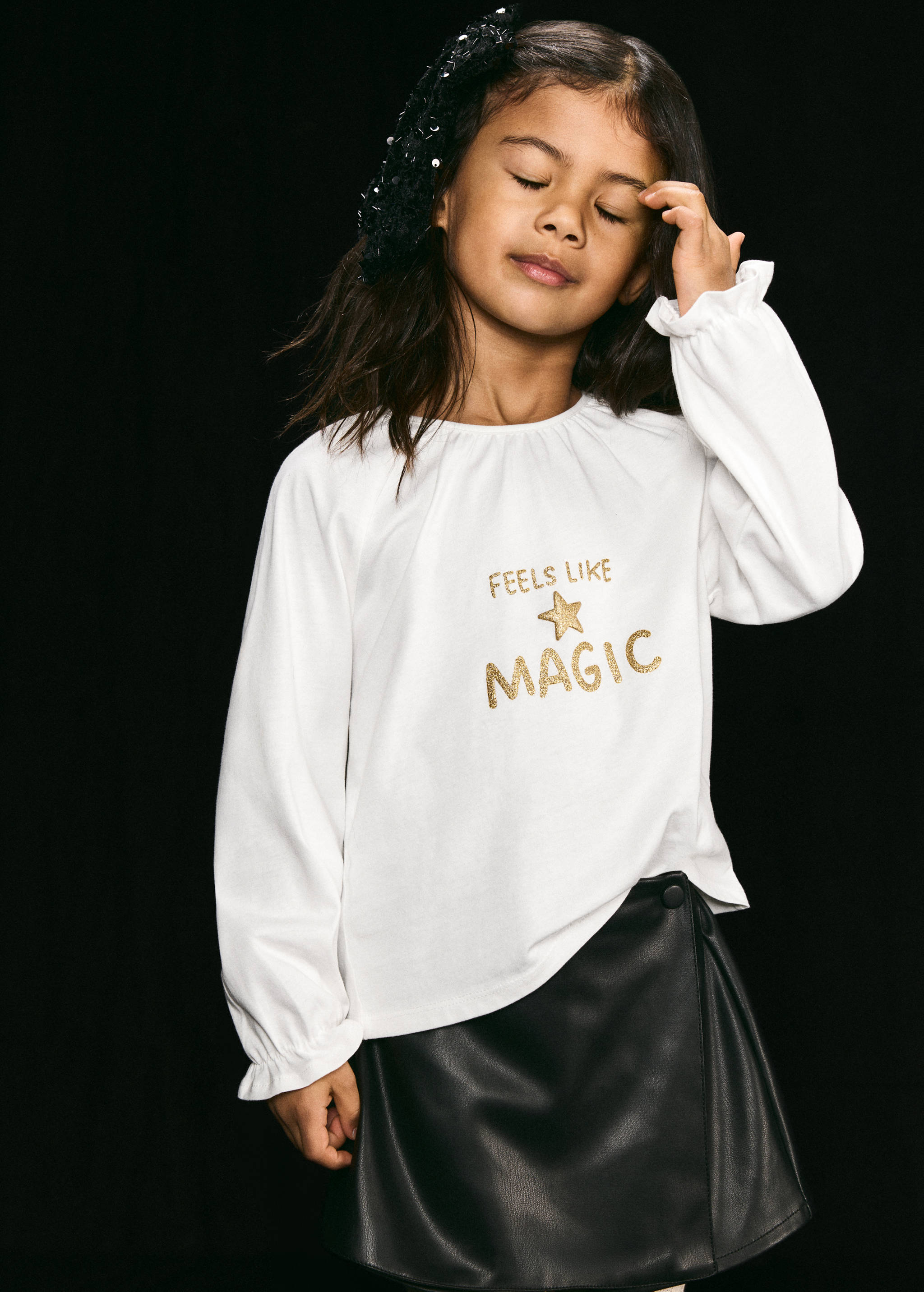 Camiseta blanca de manga larga con puños con volantes y texto de purpurina dorada.