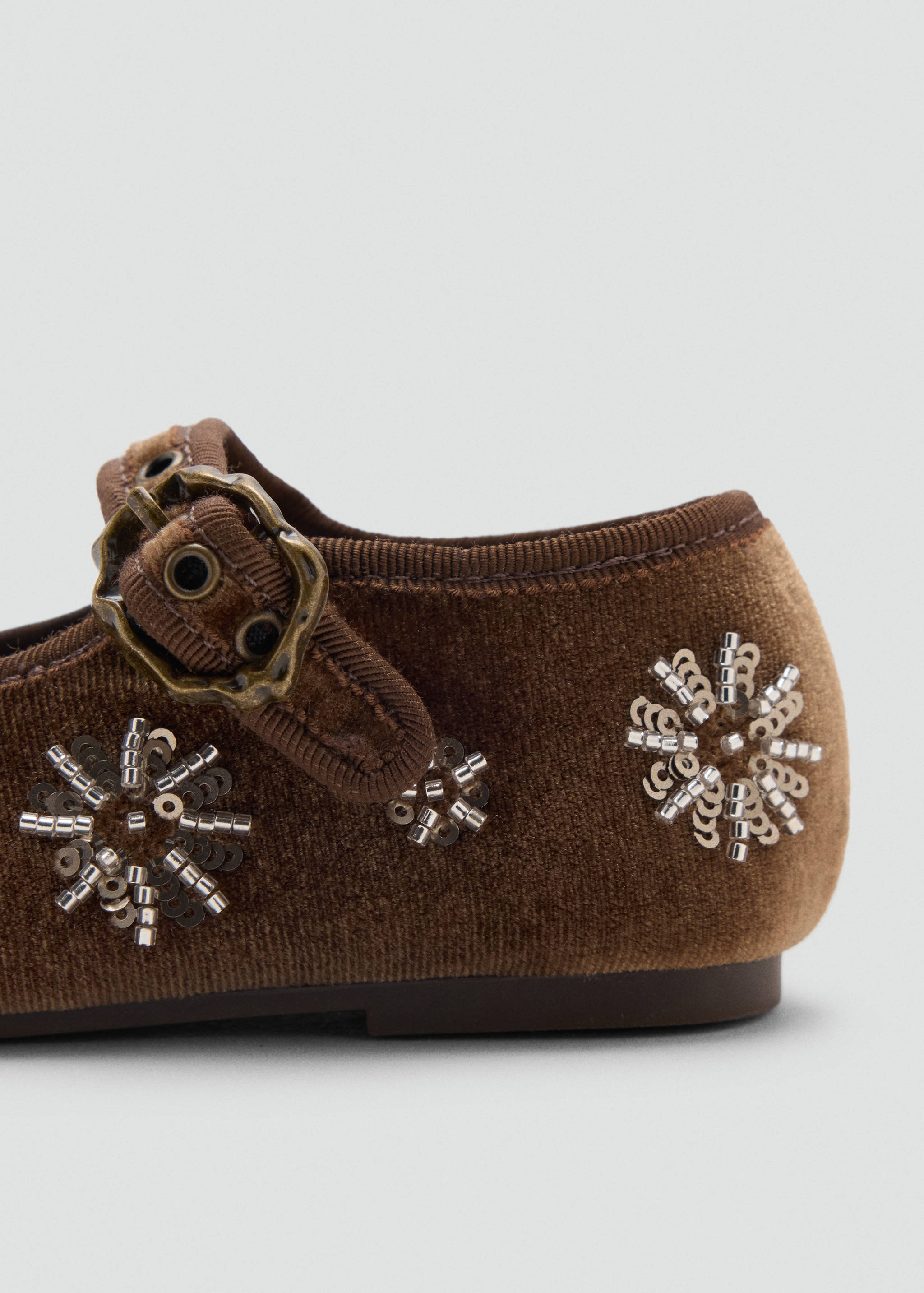 Close-up of a brown velvet shoe with a buckled strap and beaded floral embroidery.
