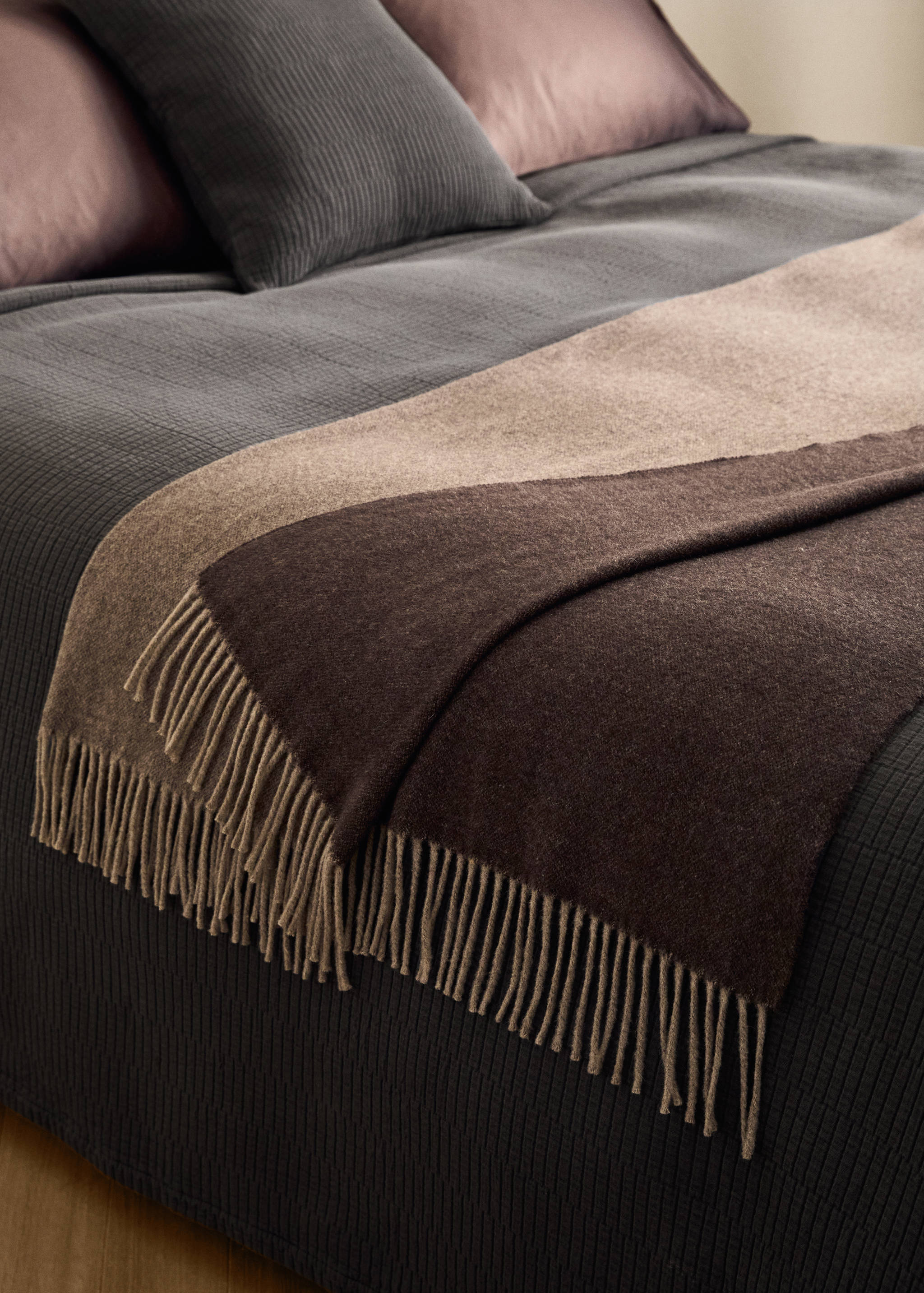 Color-blocked blanket in dark brown, taupe and beige with fringing, draped on a bed.