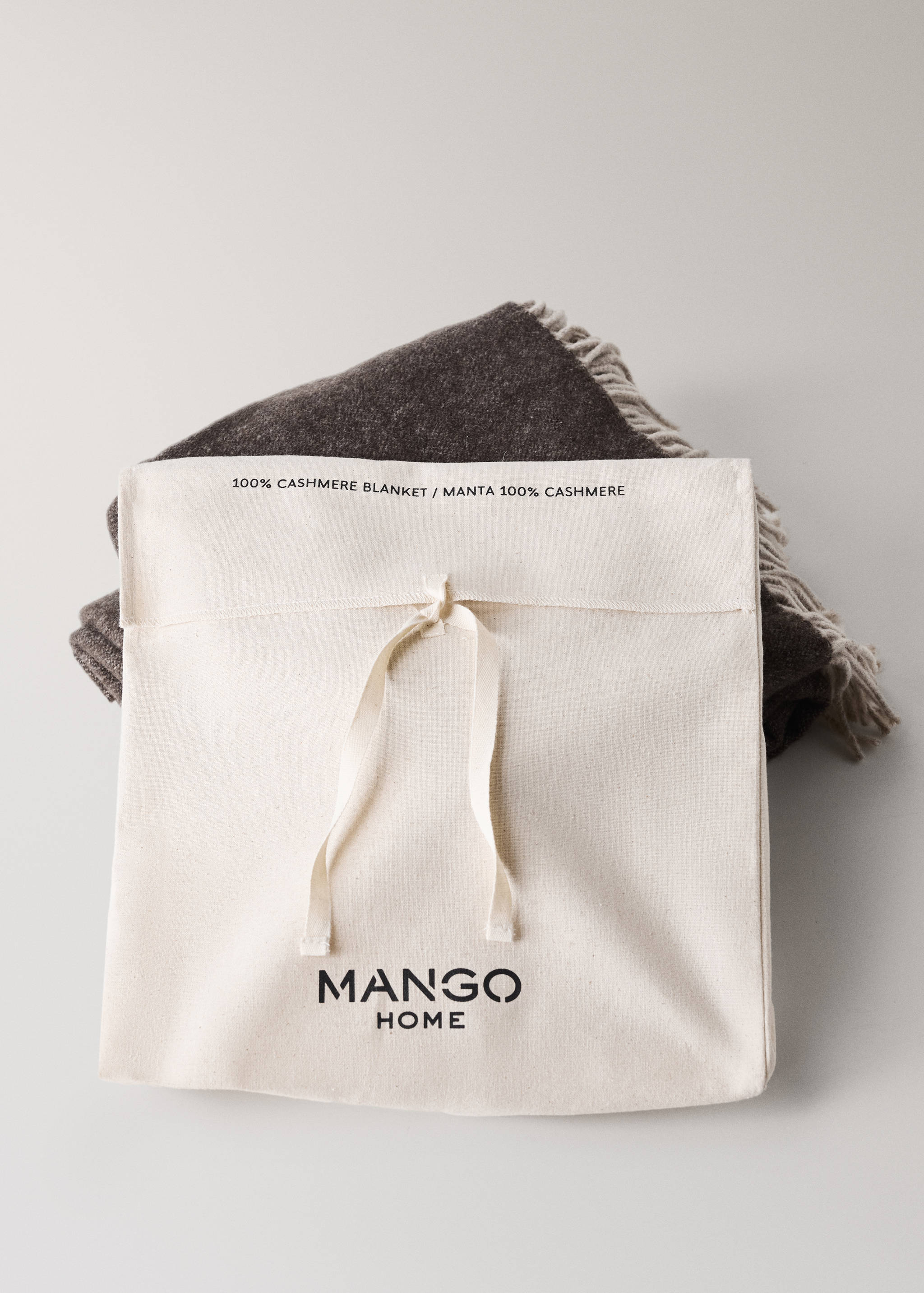 Brown cashmere blanket in a cream storage bag with Mango Home logo.