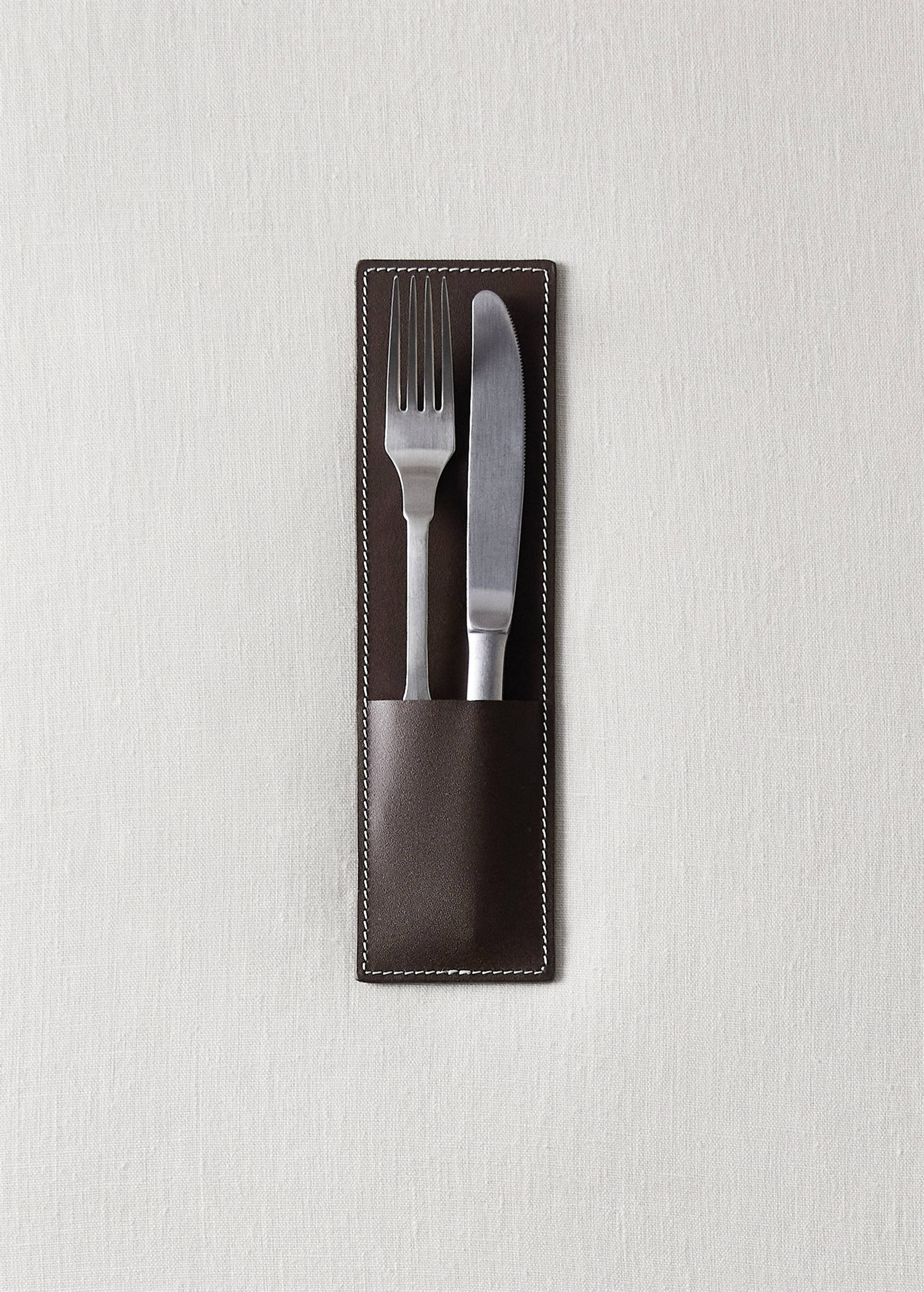 Dark brown leather cutlery holder with white stitching containing a fork and knife on linen.
