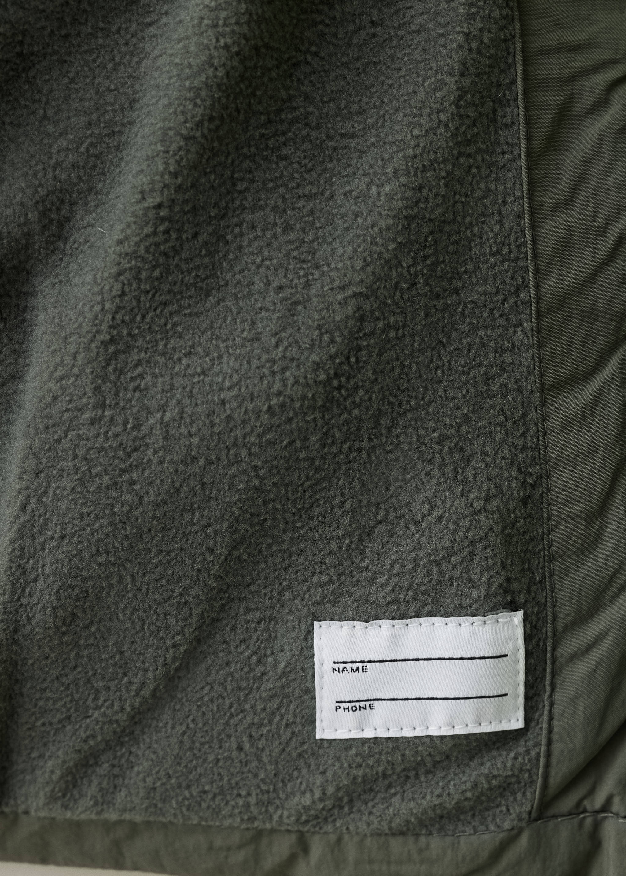 Close-up of the fleece lining and name label inside a dark green anorak.