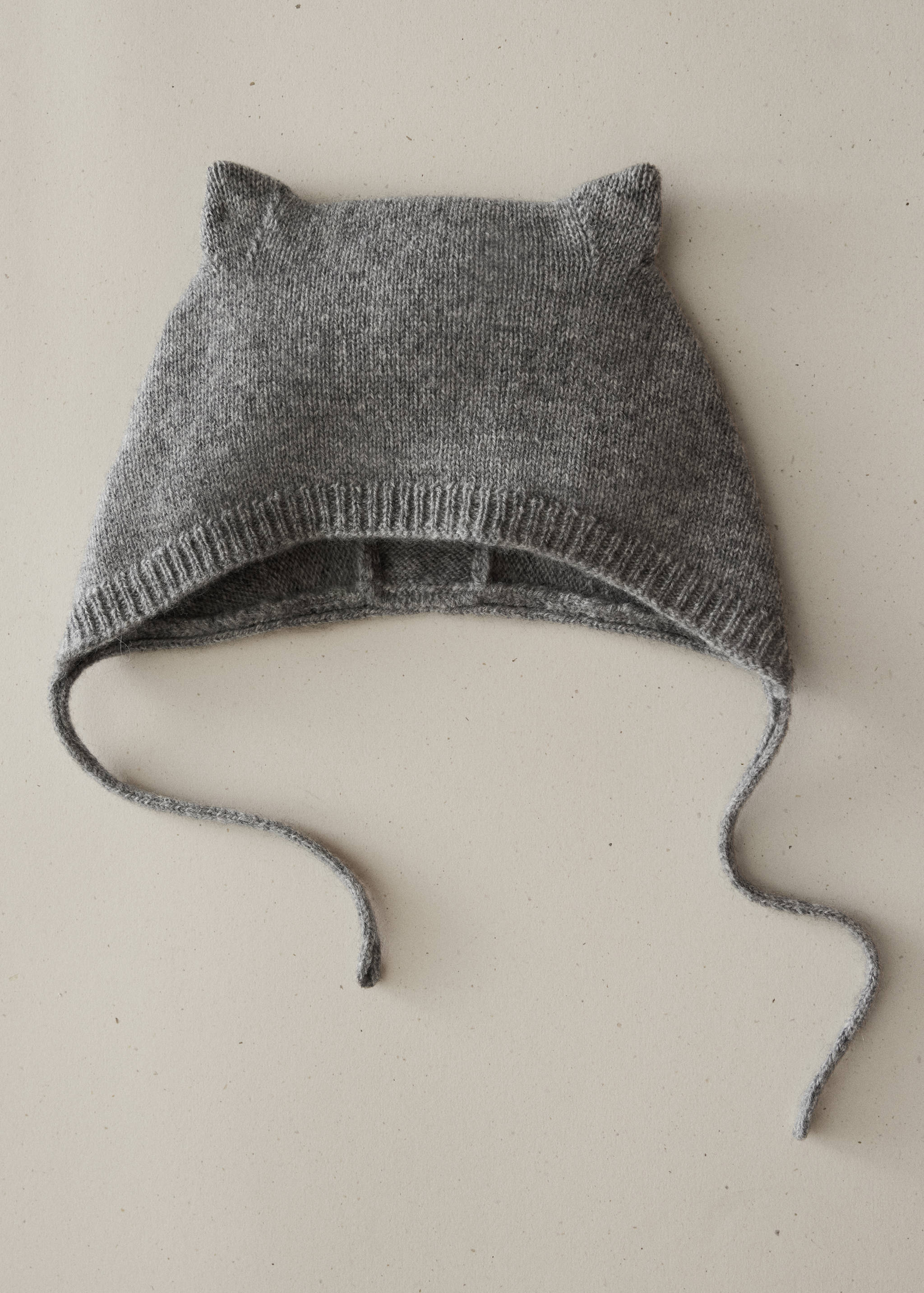 Gorro de punto para bebé de color gris con orejas de gato y cintas para atar bajo la barbilla.