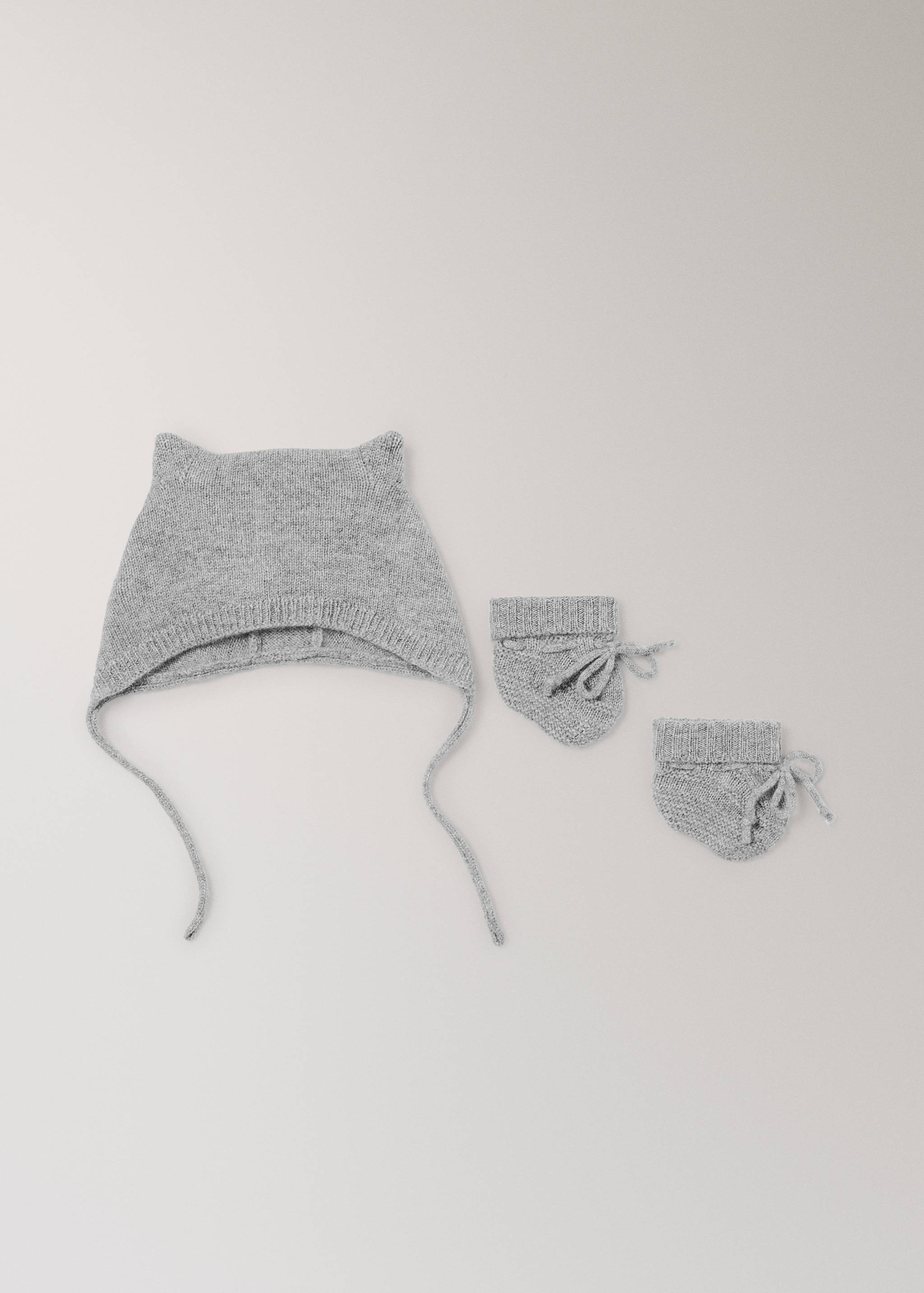 Gorro de punto para bebé en color gris con orejas y lazos, mostrado con patucos a juego.