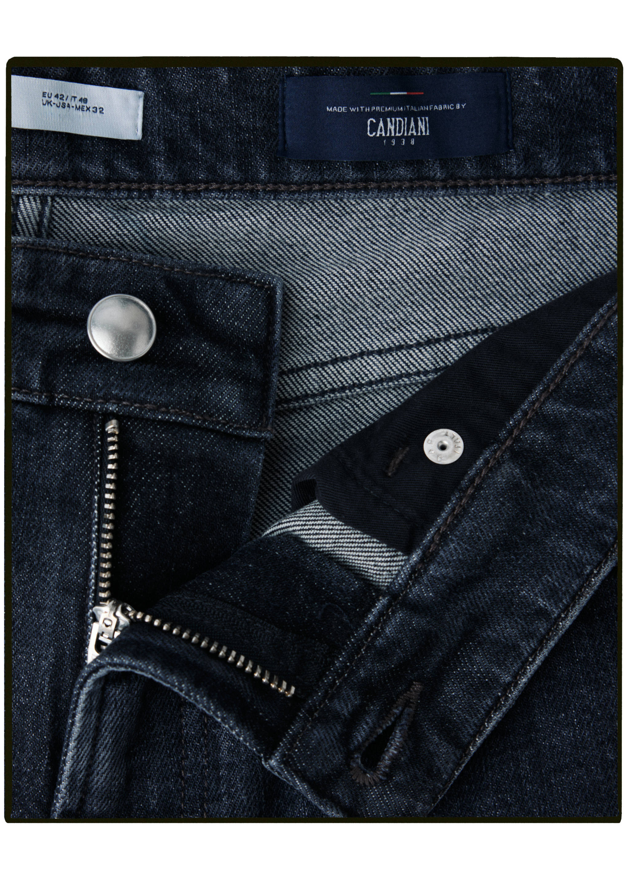 Close-up of dark blue denim trousers showing the waistband, zip fly, and Candiani label.
