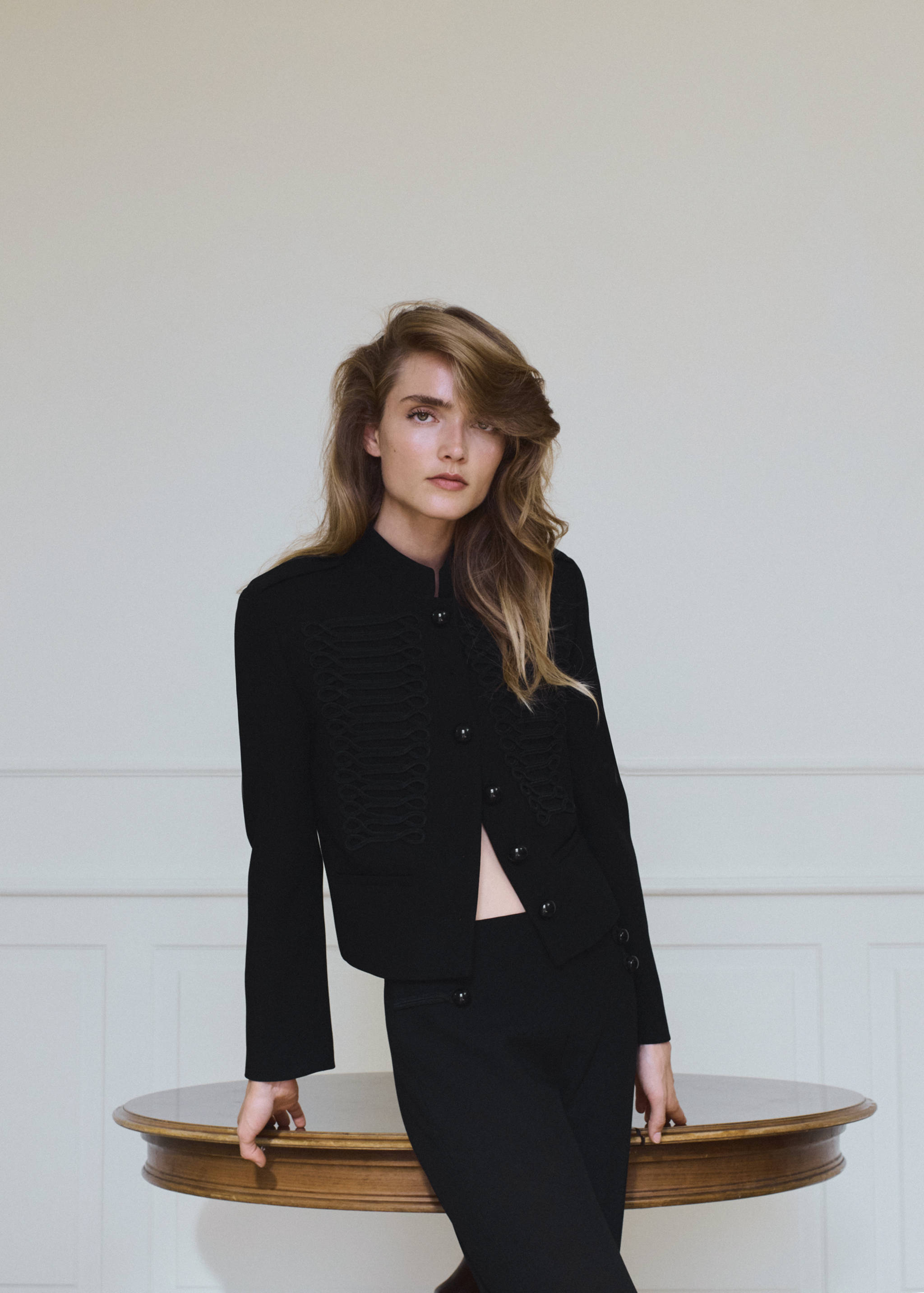 Black cropped military jacket with stand collar and decorative braiding.