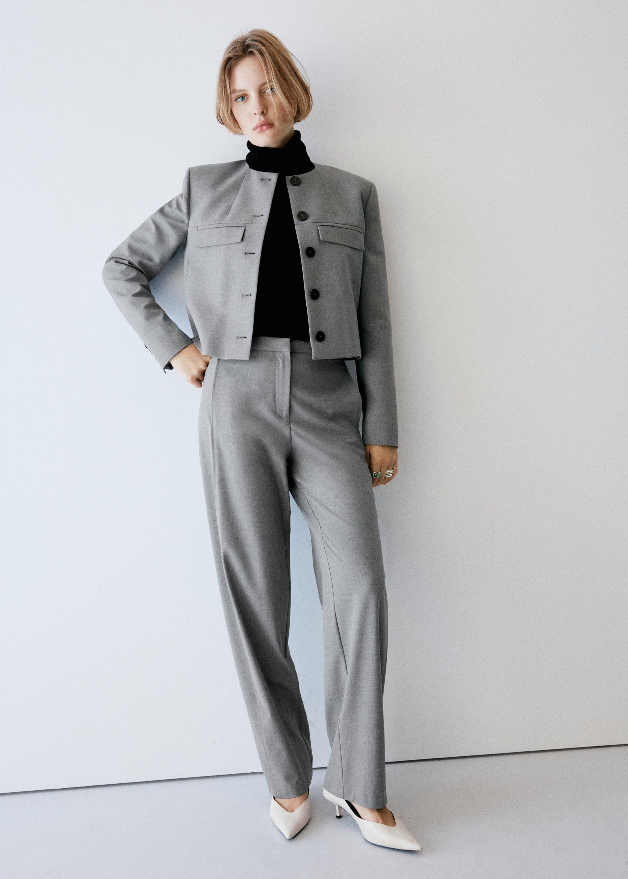 Grey trousers styled with a matching cropped jacket, black turtleneck, and white heels.