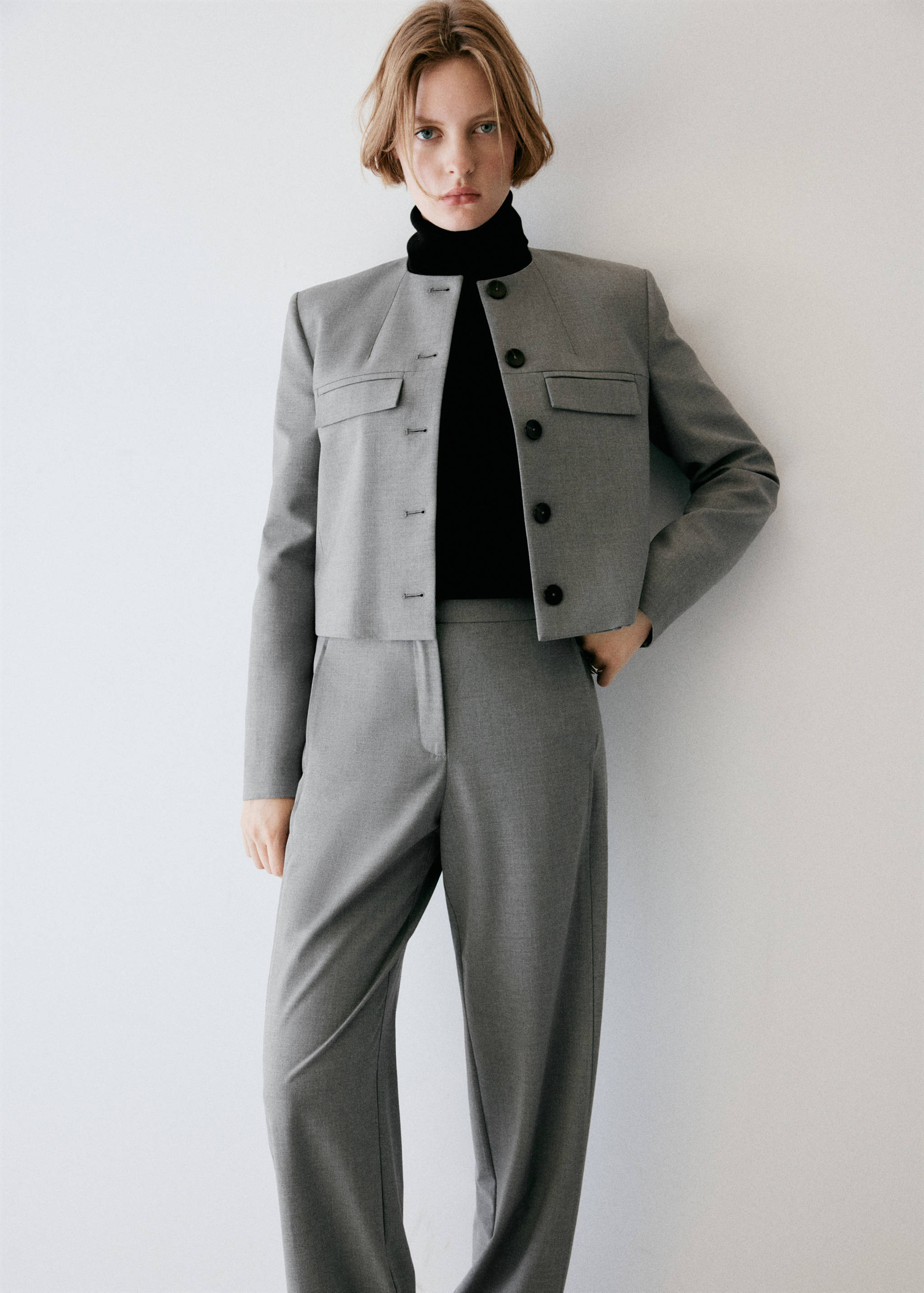 Grey trousers with a straight-leg fit, worn with a matching grey cropped jacket and black turtleneck.