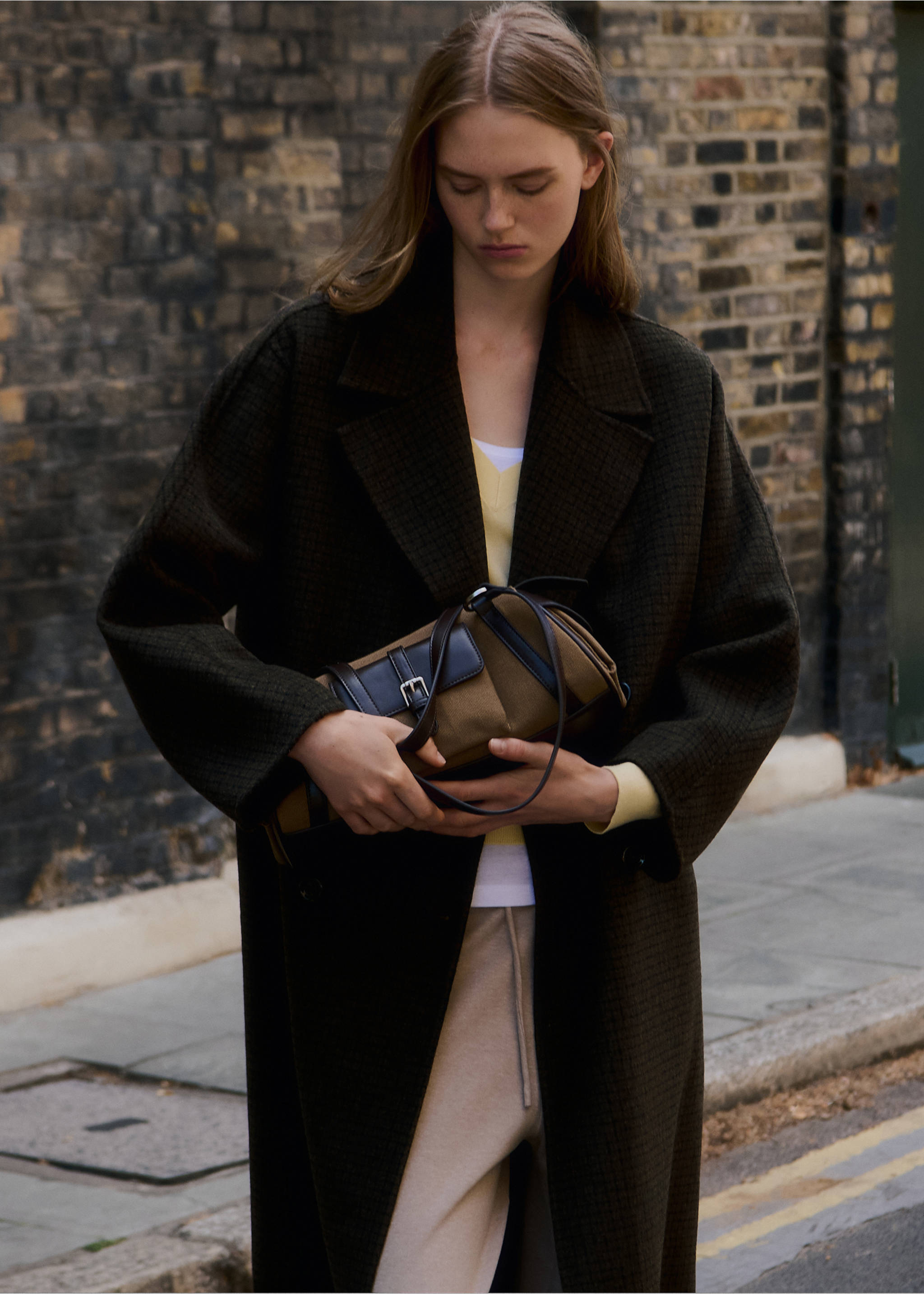 Brown and black shoulder bag with a front flap and buckle detail, held by a model., Khaki. Ref: 37036010-00.