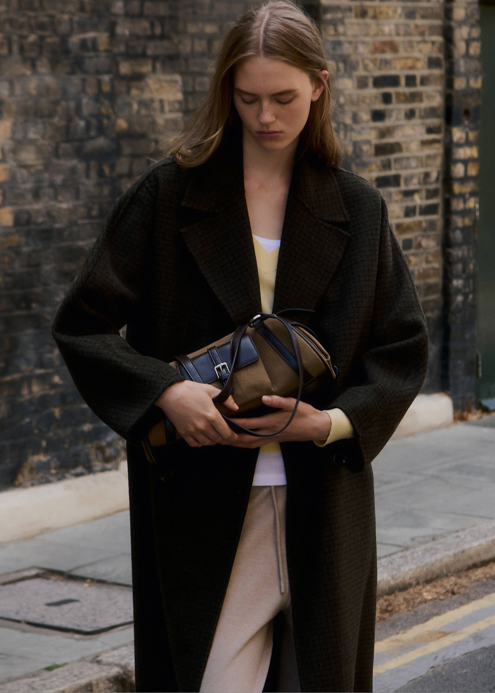 Brown and black shoulder bag with a front flap and buckle detail, held by a model.