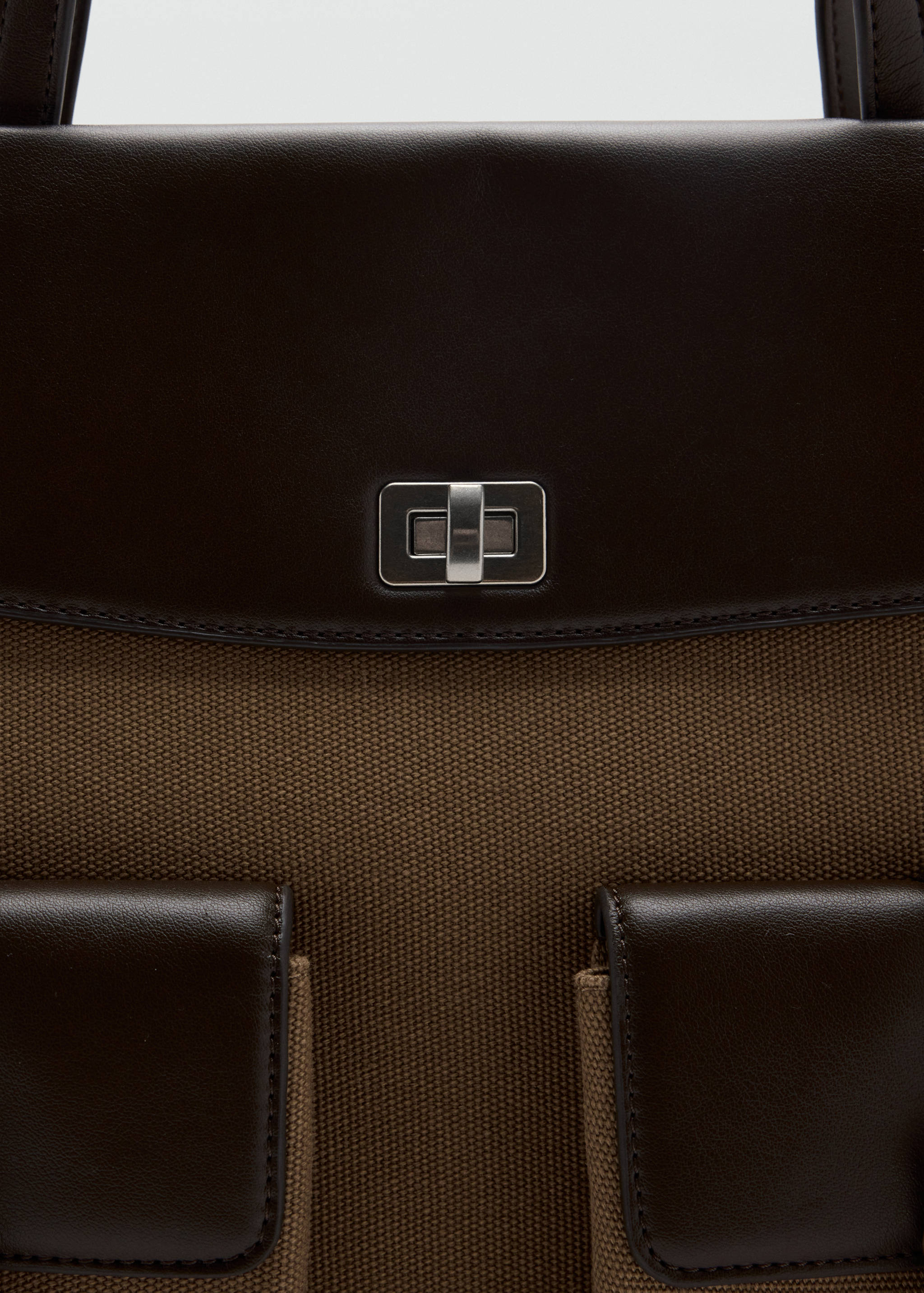Close-up of a dark brown and khaki tote bag with a turn-lock closure.