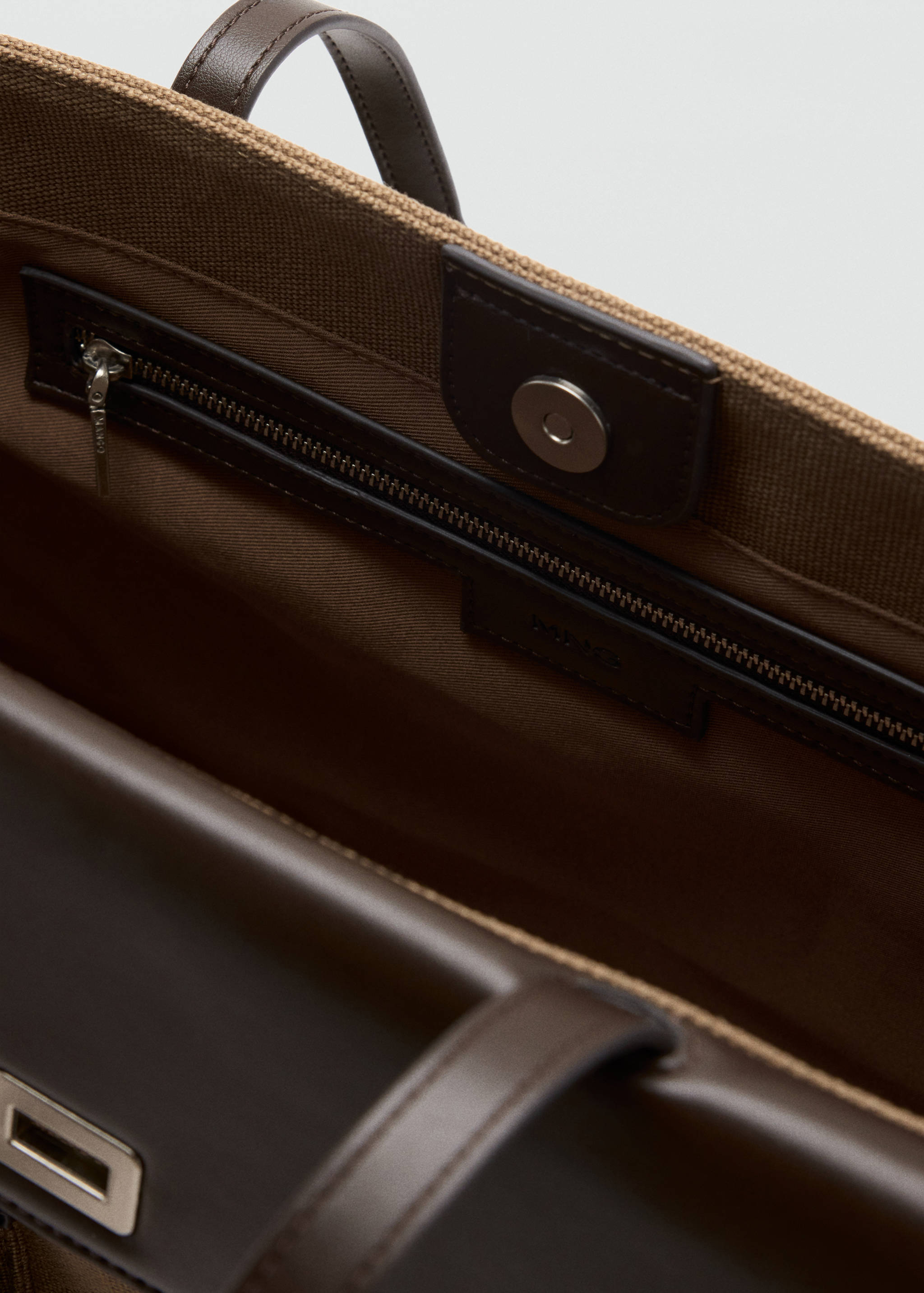 Close-up of the interior of a brown tote bag showing the zipped pocket and snap closure.