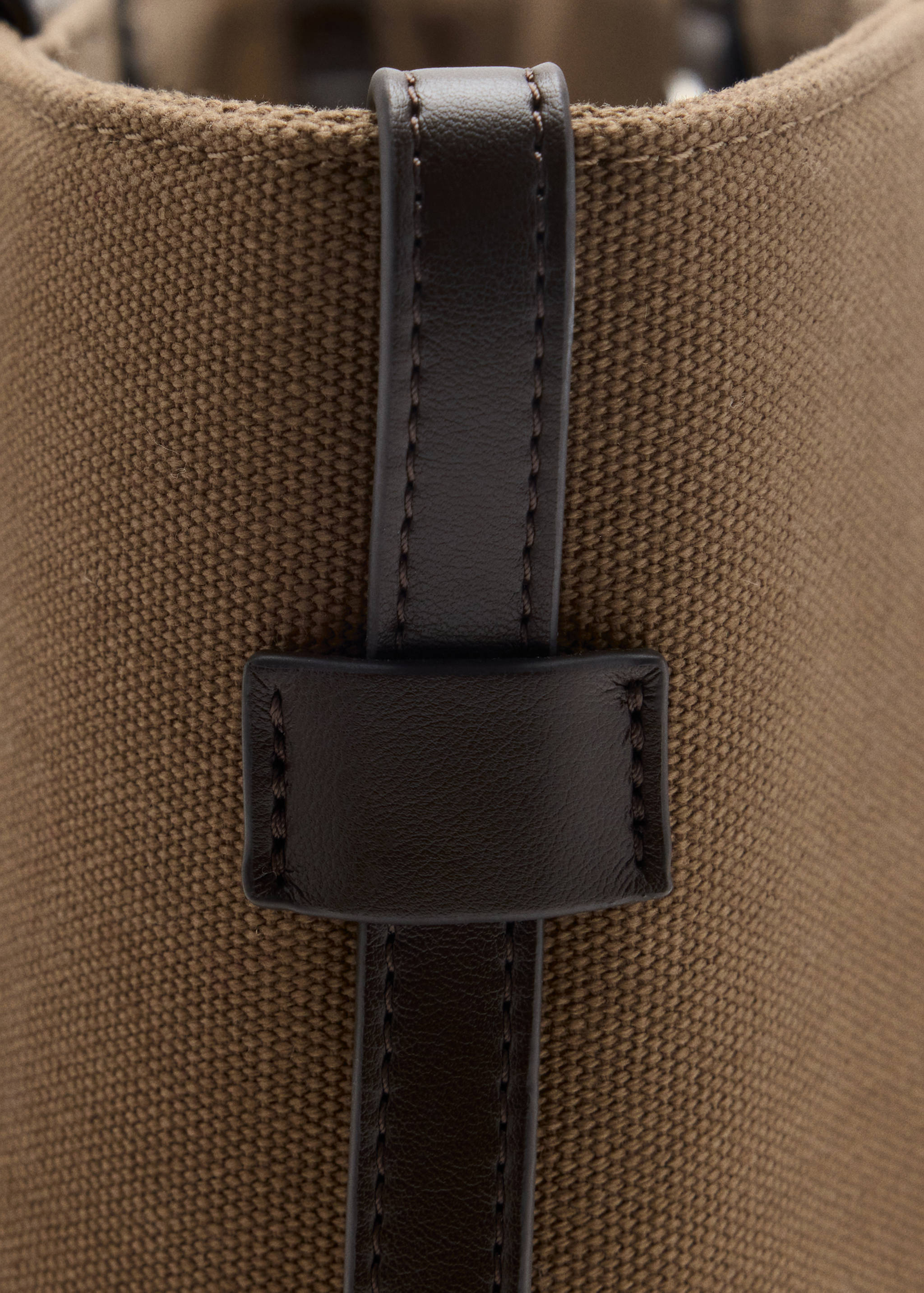 Close-up of a brown canvas tote bag with a dark brown leather strap detail.