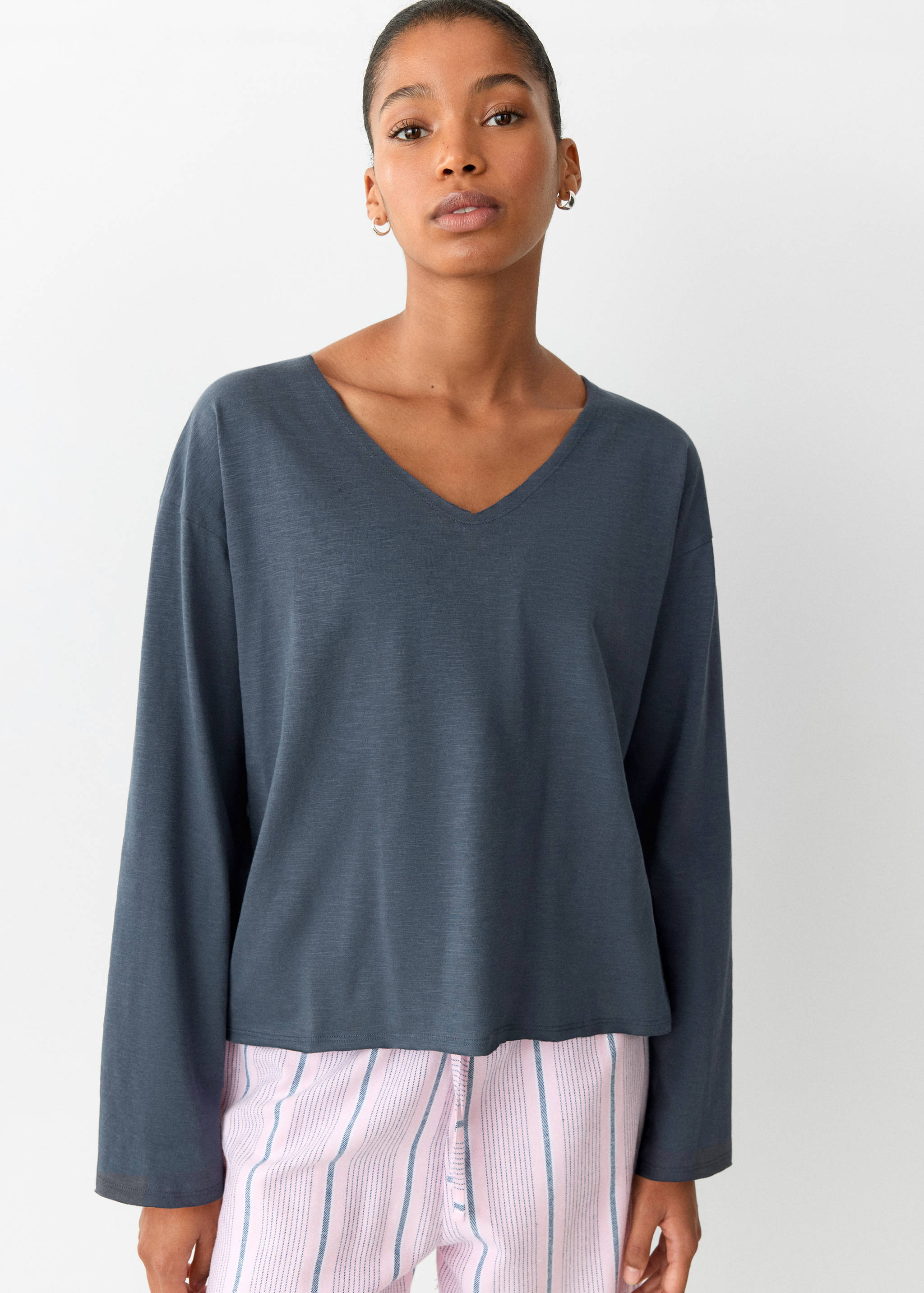 Dark grey V-neck pyjama top with long sleeves, worn with striped trousers.