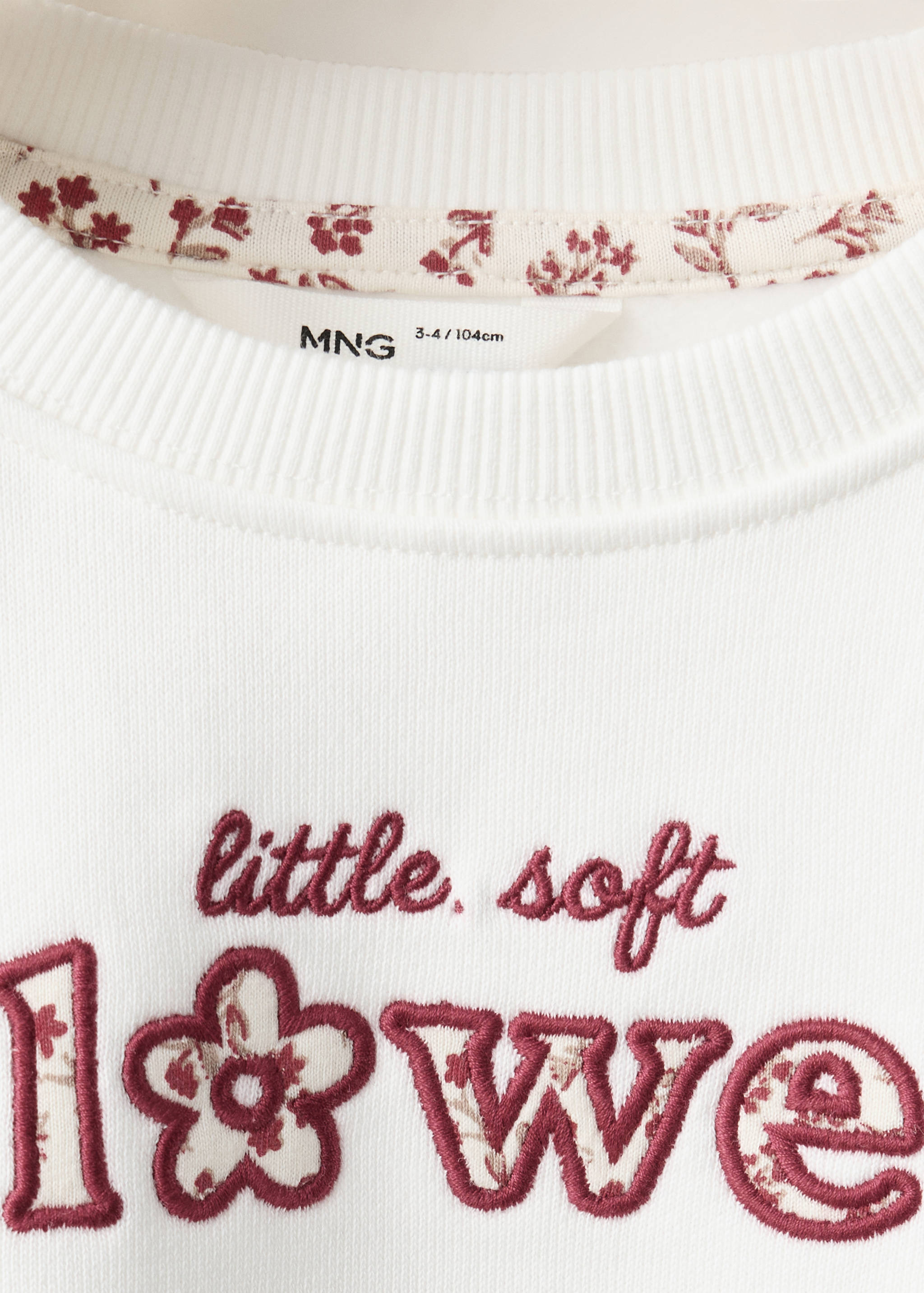 Off-white sweatshirt detail with a floral-trimmed collar and red chest embroidery.
