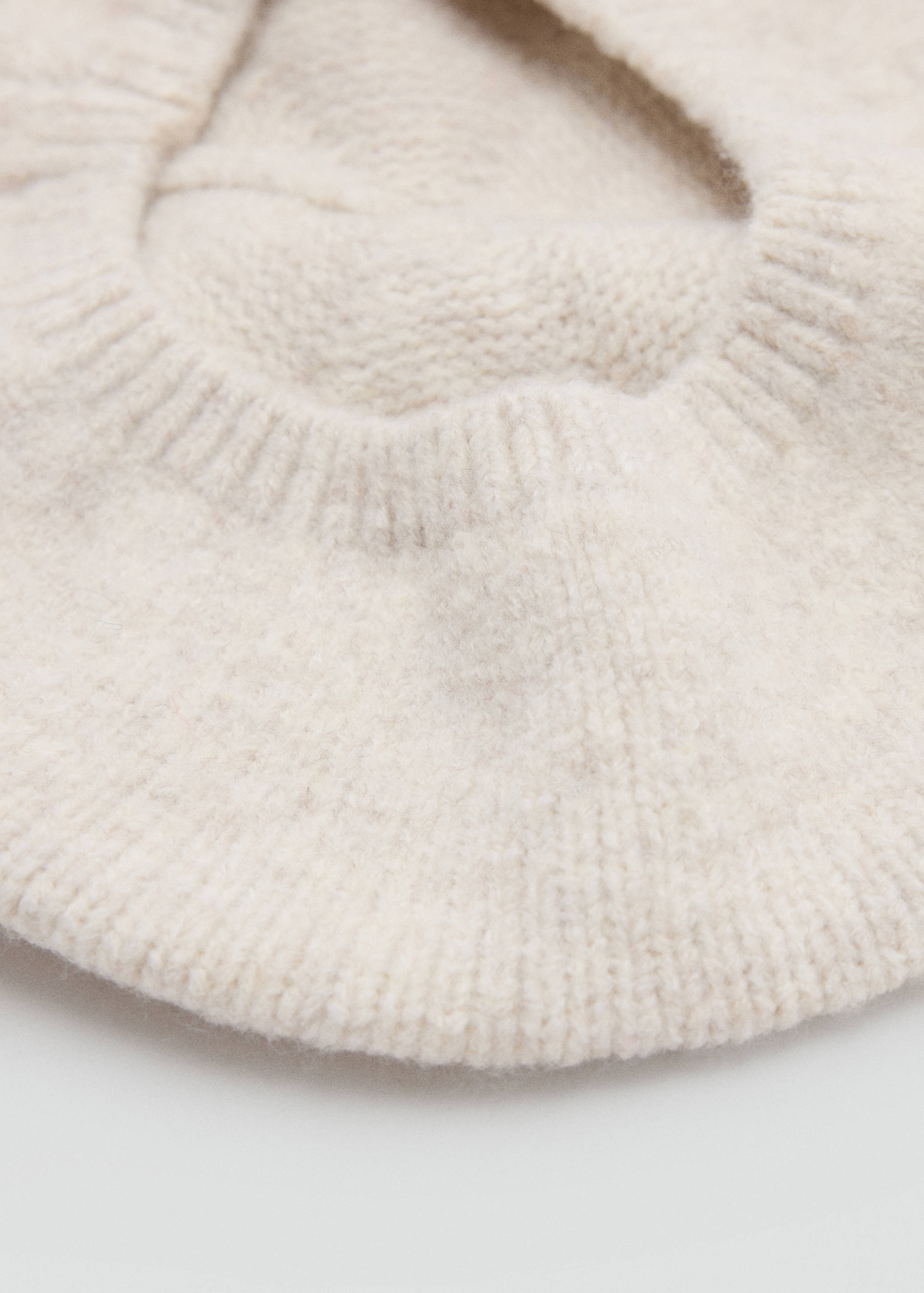 Close-up of a soft off-white knitted beanie highlighting its textured ribbed knit.