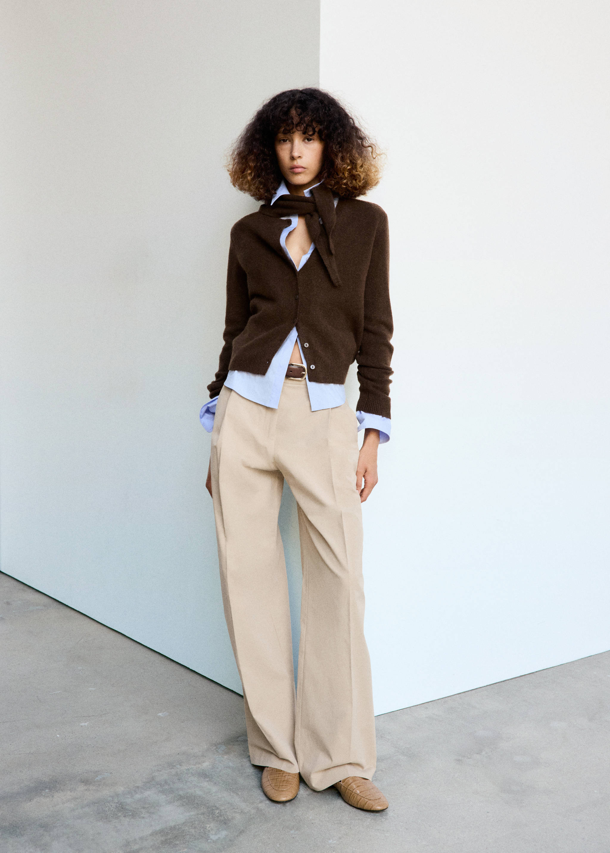 Brown cardigan with a matching tied scarf, worn over a blue shirt and beige trousers.