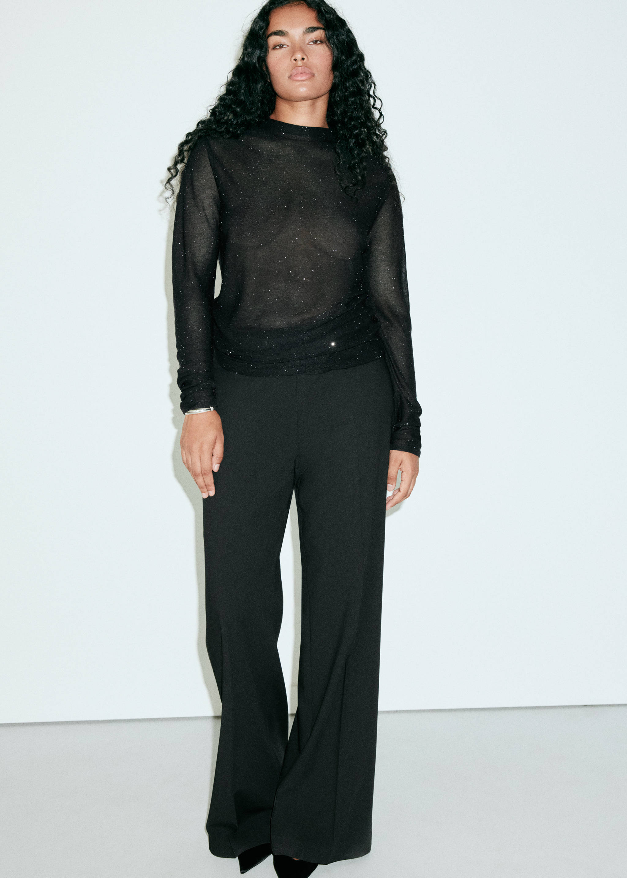 Black sheer glitter long-sleeved top with a round neckline, worn with black trousers.