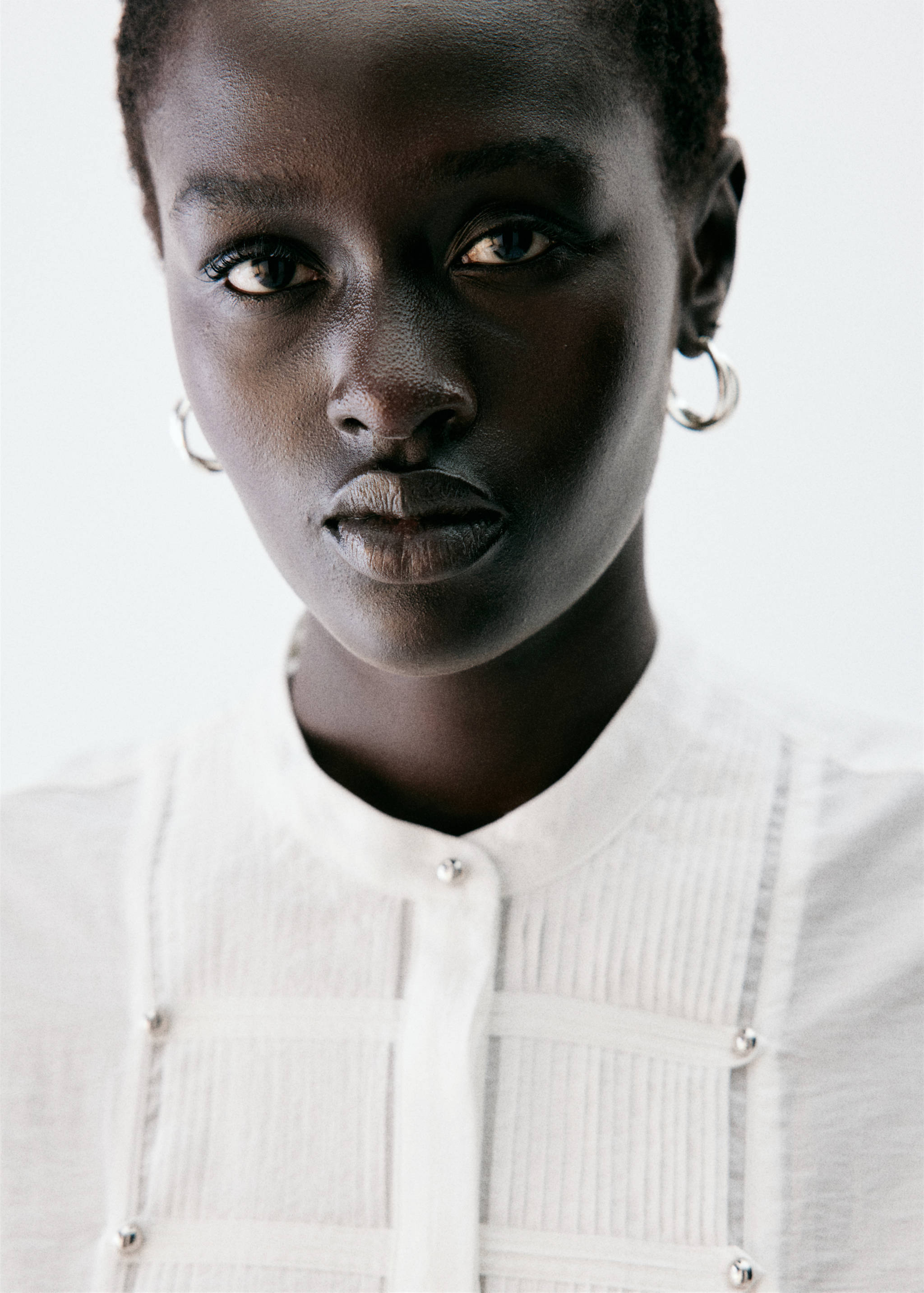 Close-up of a white blouse with a mandarin collar and decorative metallic button details.