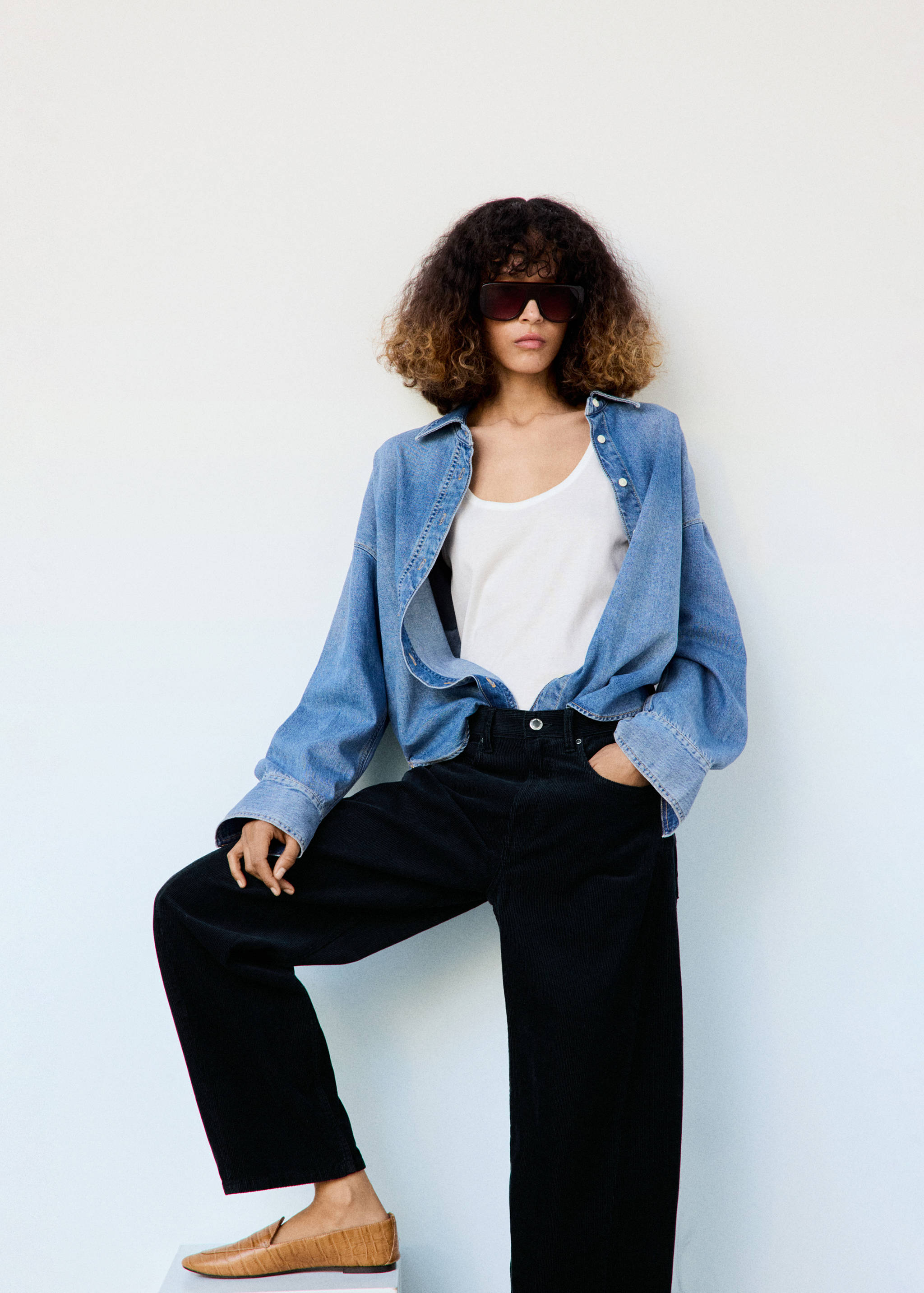 Blue denim shirt worn unbuttoned over a white top with black trousers.