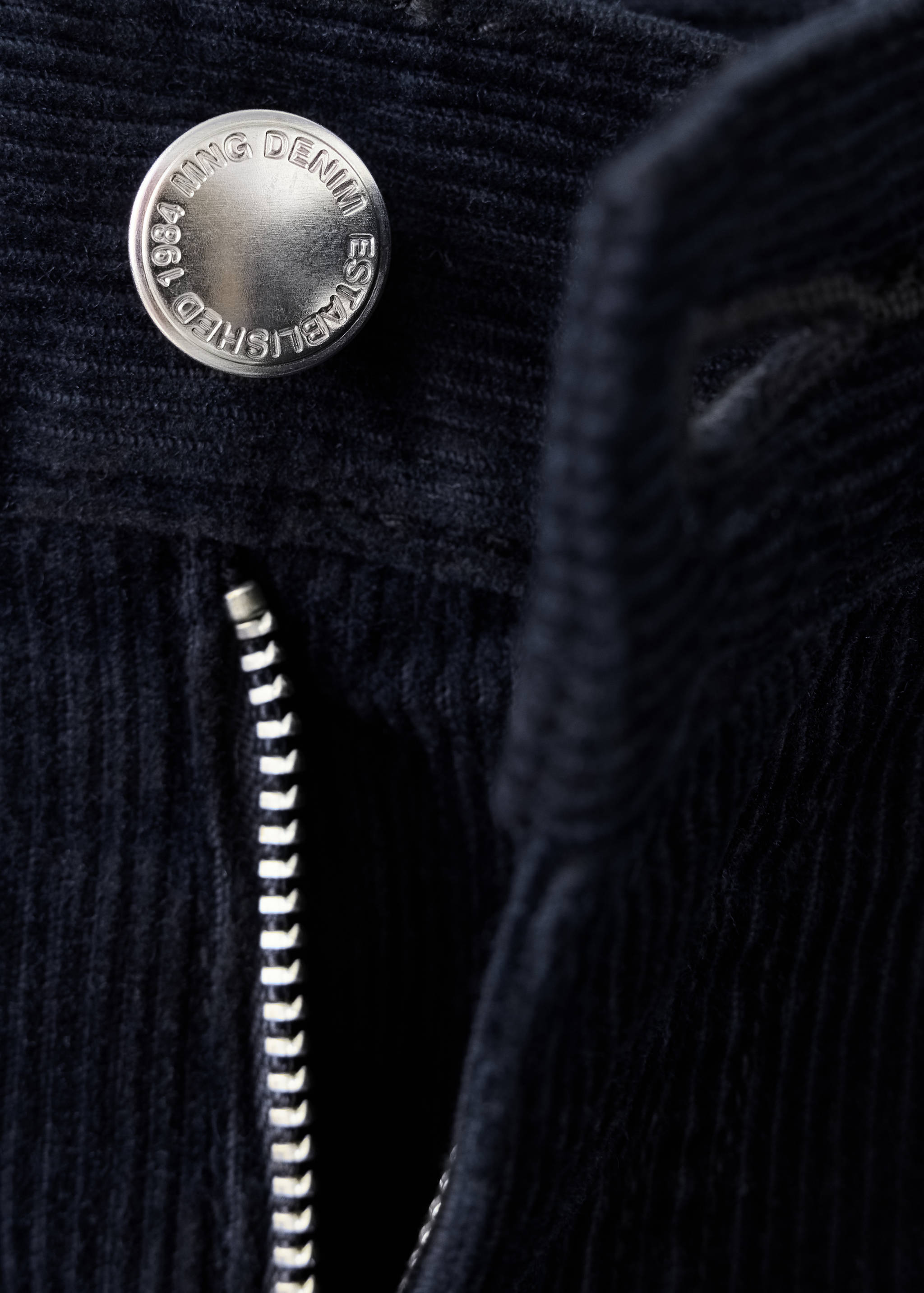 Close-up of navy corduroy trousers button and zip detail.