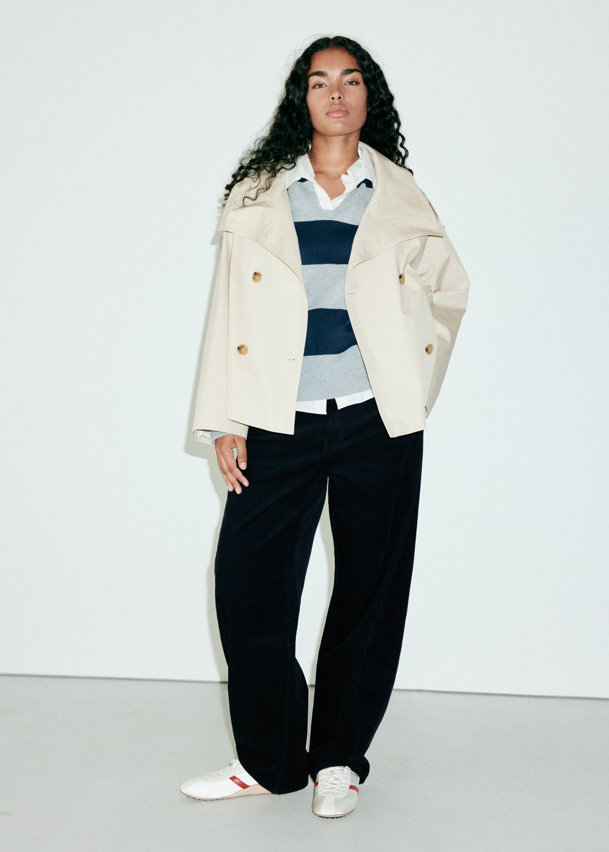 Black wide-leg trousers worn with a beige double-breasted jacket and striped sweater.