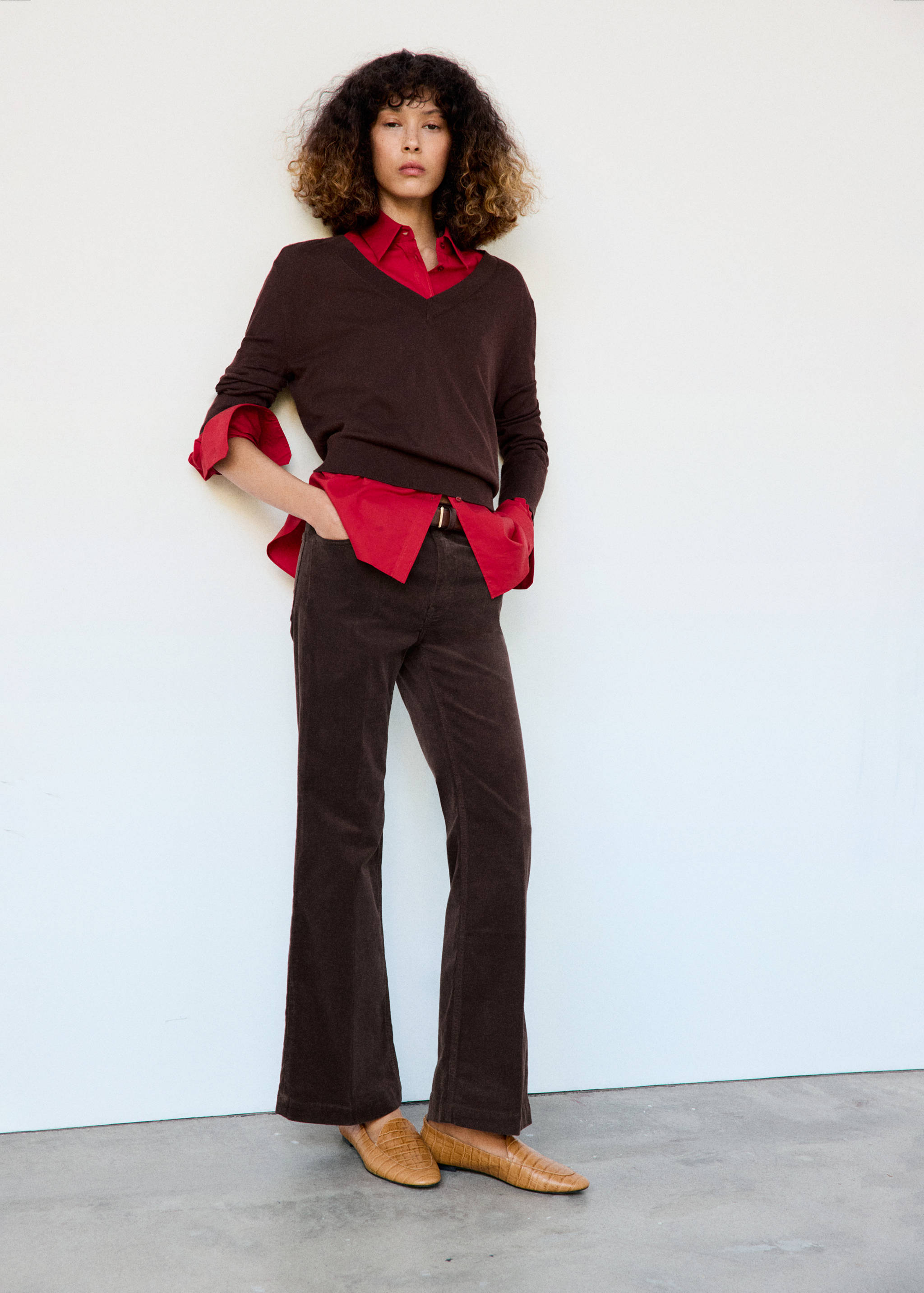 Dark brown corduroy trousers worn with a red shirt and brown V-neck sweater.