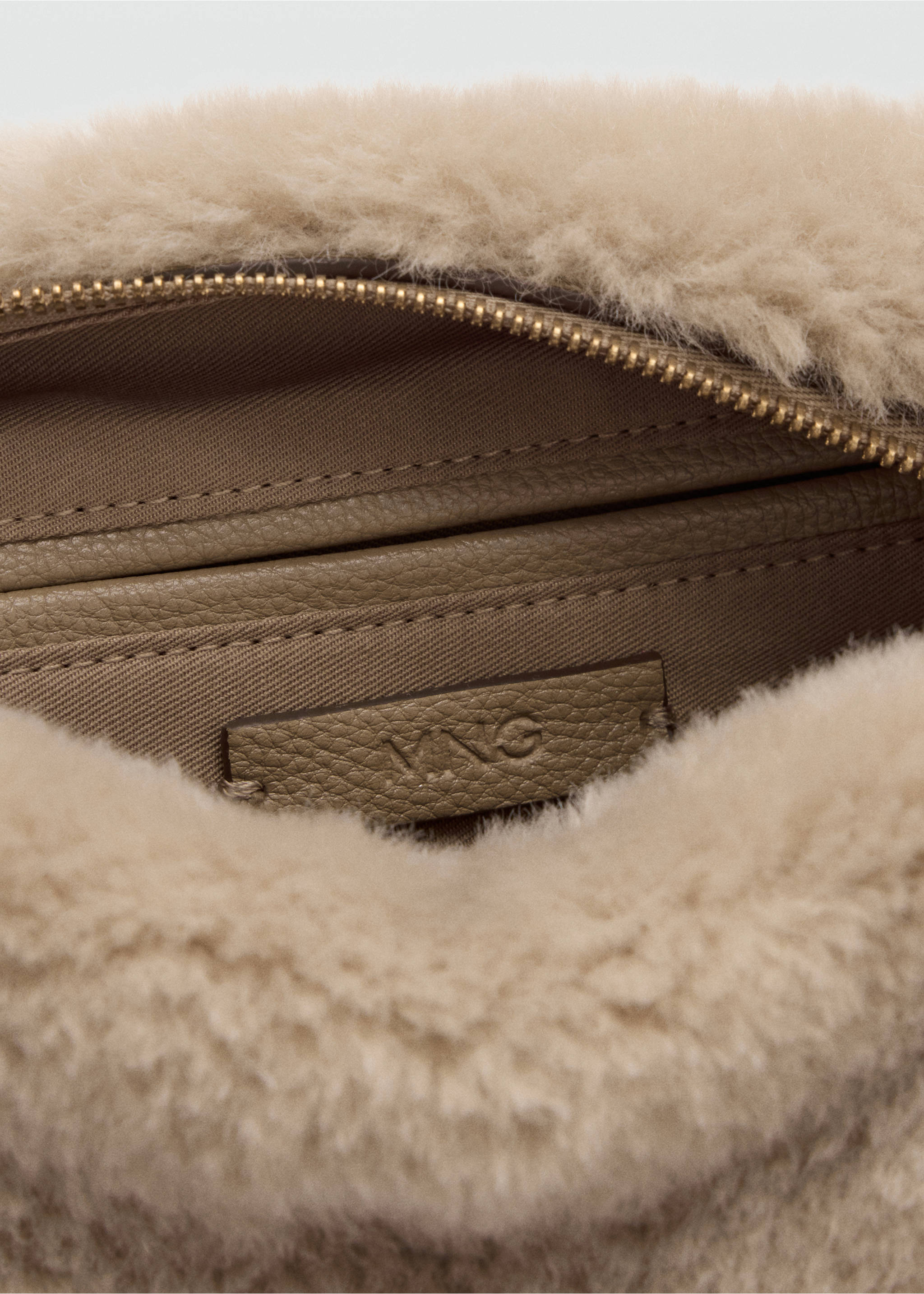 Primer plano del interior de un bolso saco de borreguillo sintético beige, que muestra la cremallera y la etiqueta de la marca., Beige. Ref: 37037798-00.