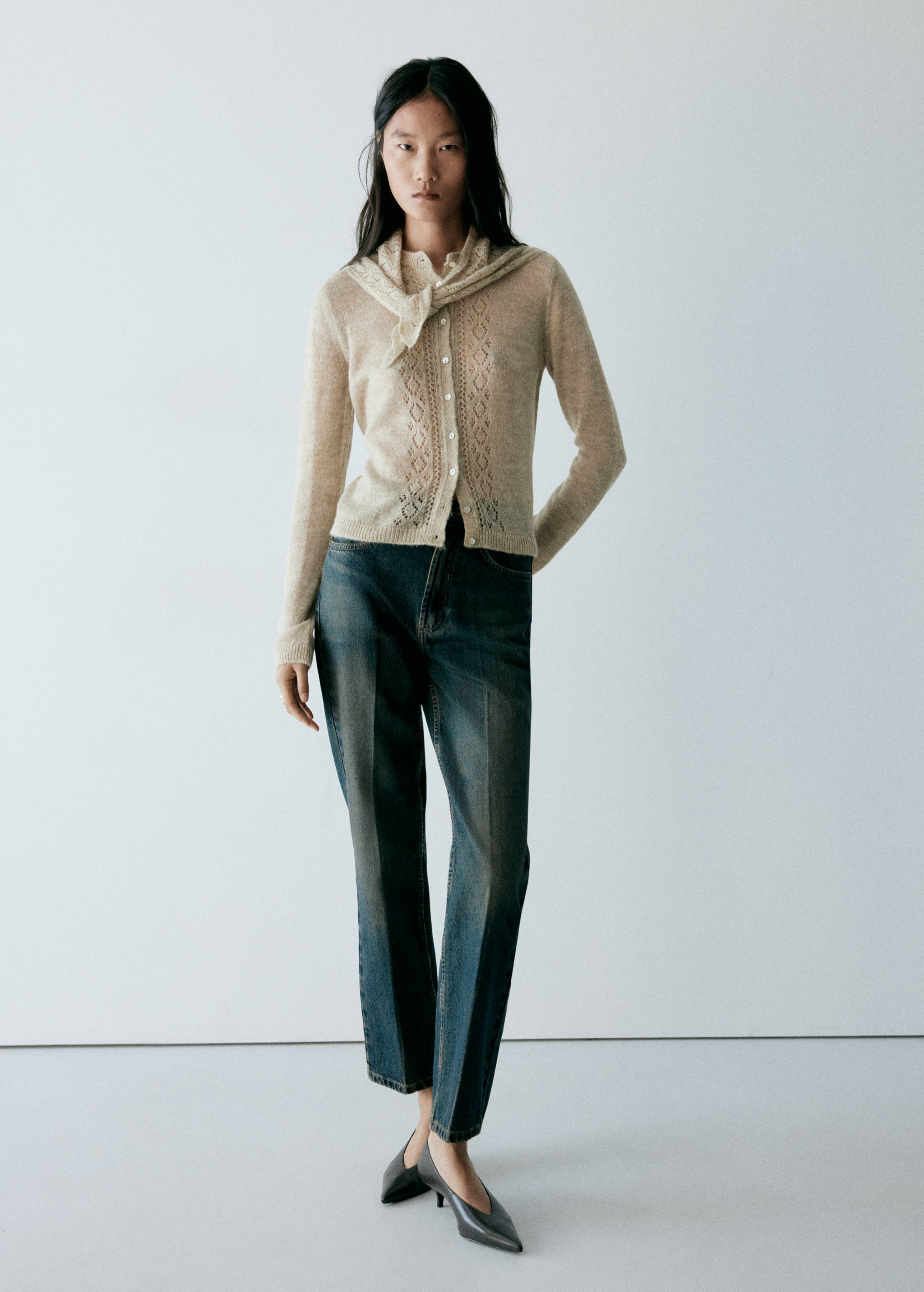 Beige knitted cardigan with openwork details and a matching sweater draped over the shoulders.