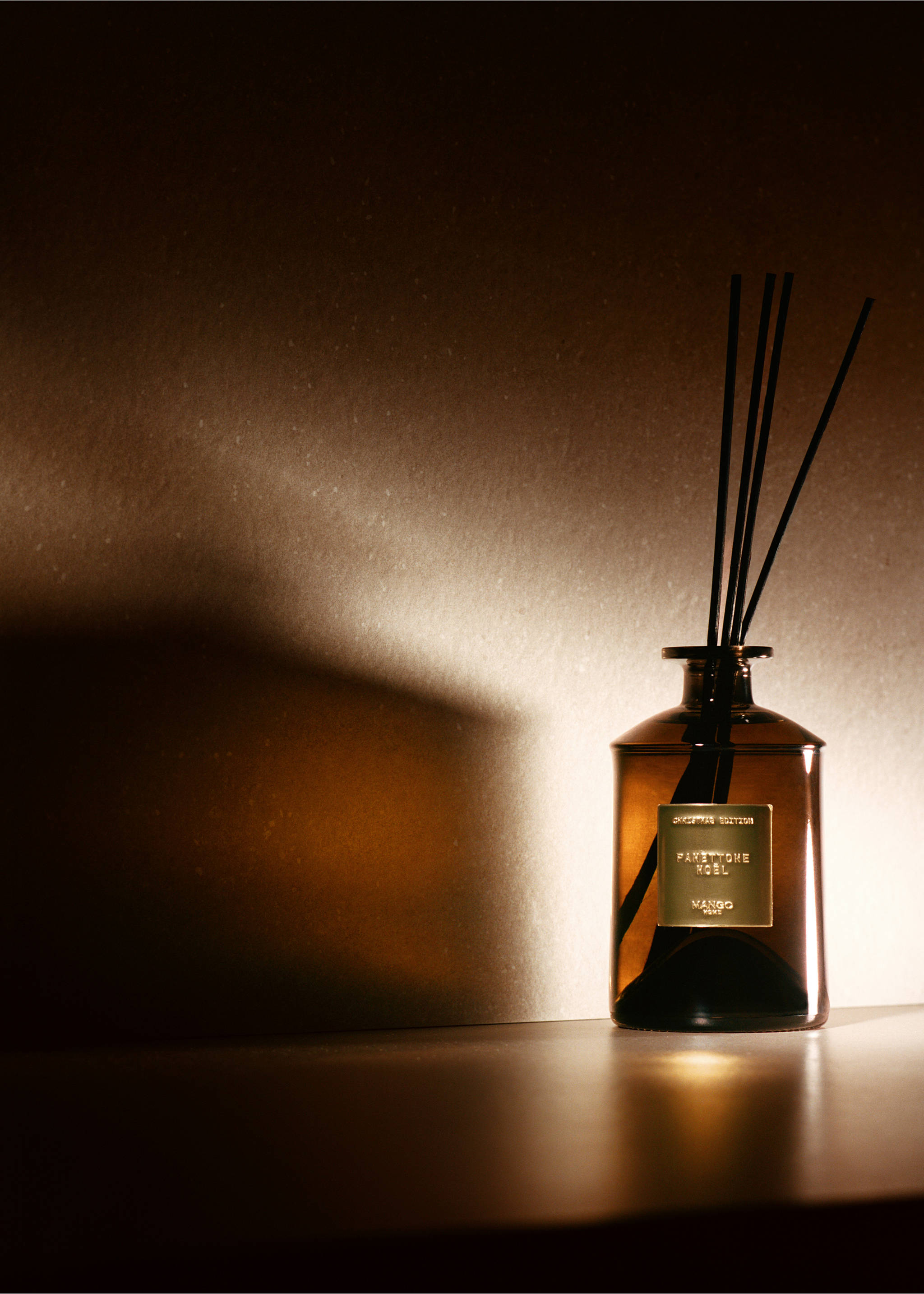 Brown glass reed diffuser bottle with black reeds and a gold-coloured label on a dark surface., Gold. Ref: 37037815-00.