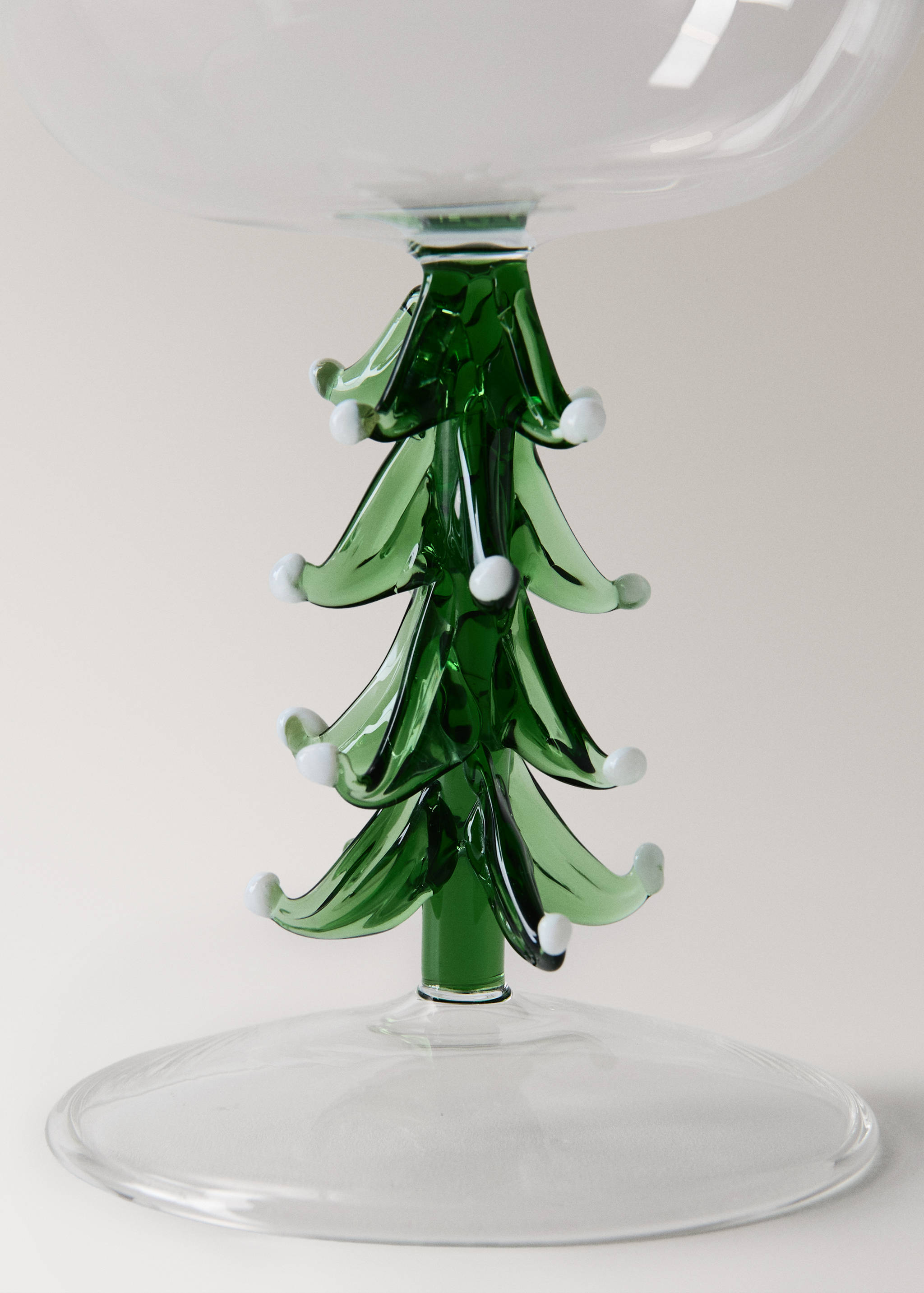 Close-up of a glass goblet with a decorative green Christmas tree stem with white tips.
